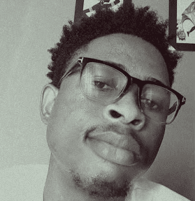 A person with glasses and curly hair is looking slightly upwards in a casual setting.