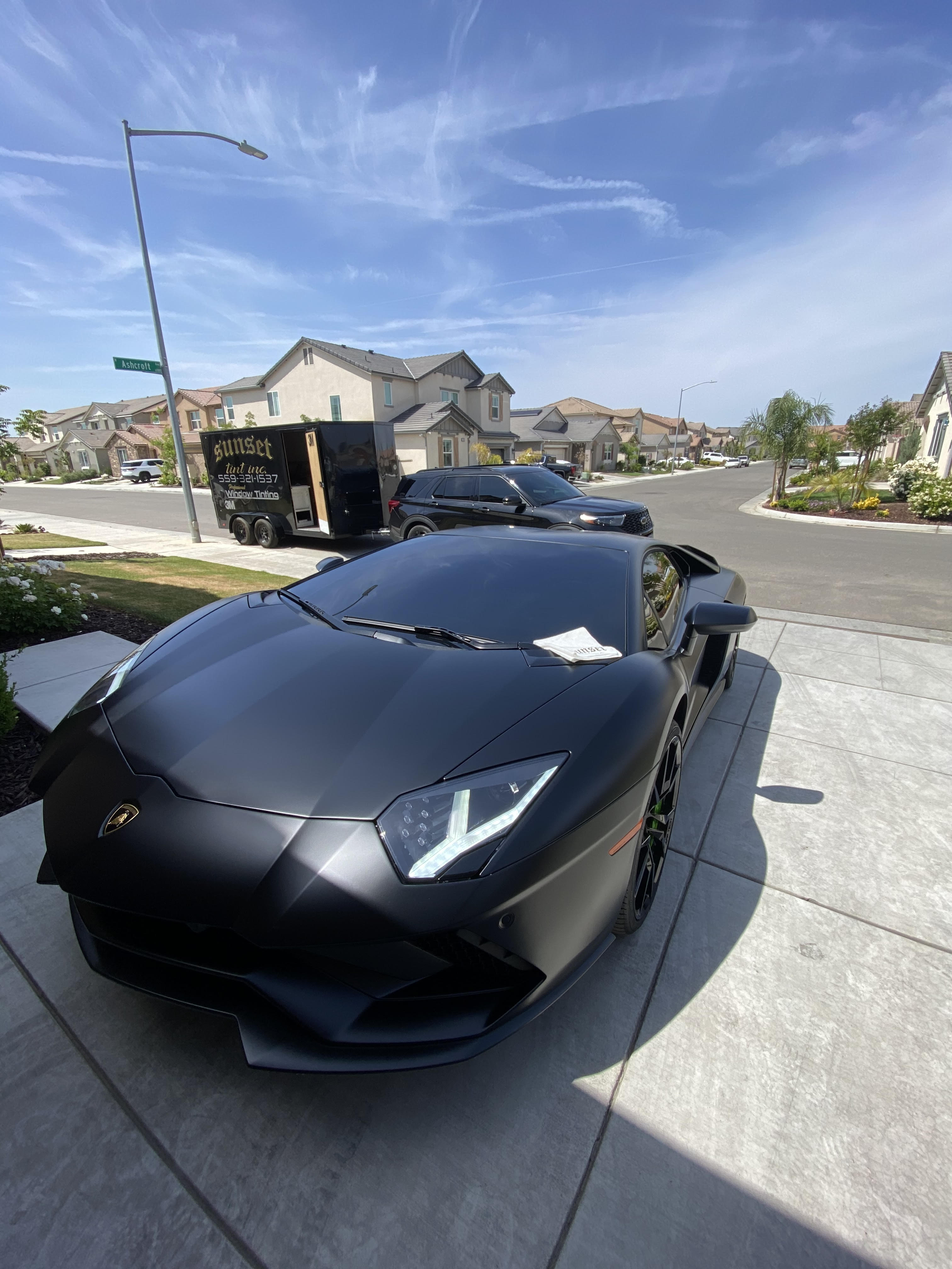 Two people in a workshop, one standing and smiling while the other leans over a car, working on it.