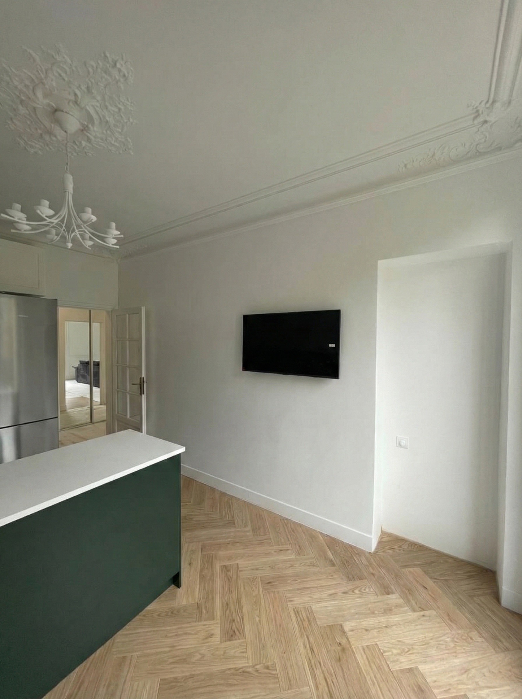 Vue sur l'espace cuisine moderne intégrée avec des touches de vert forêt dans un intérieur parisien classique.