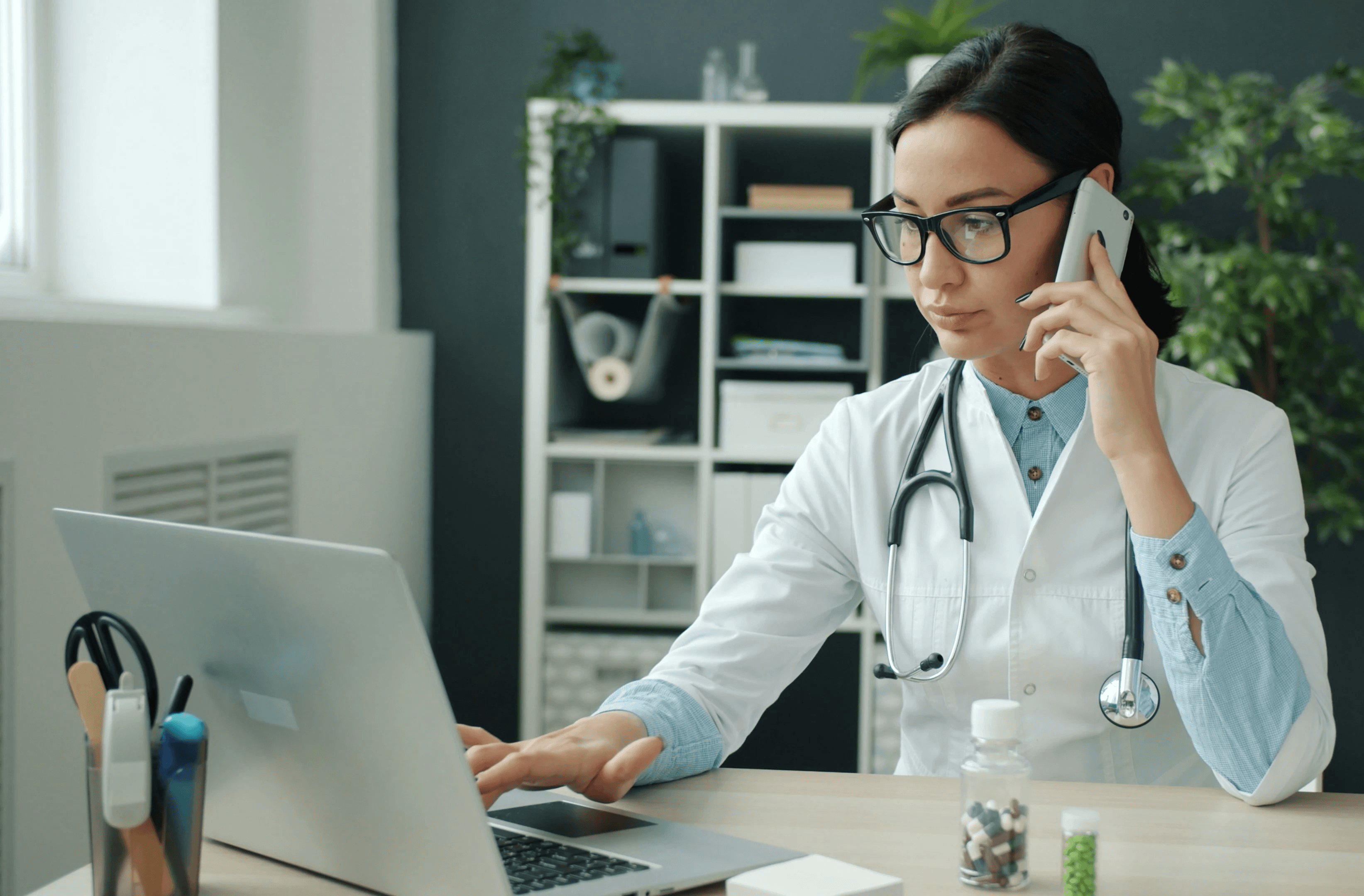 Doctor on phone, working on laptop in office.