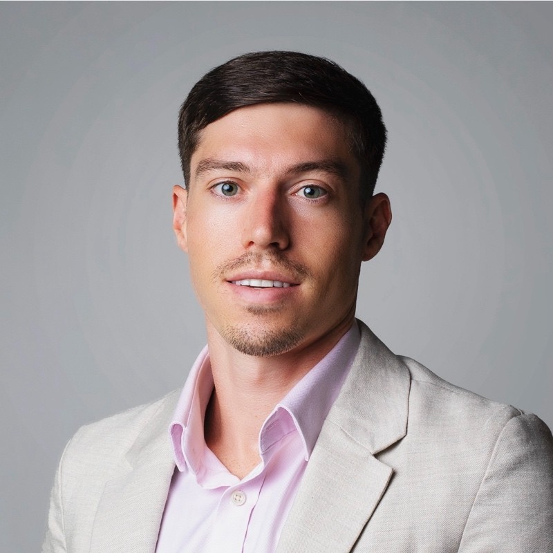 Fictional team member portrait of a man in dark blazer on dark background