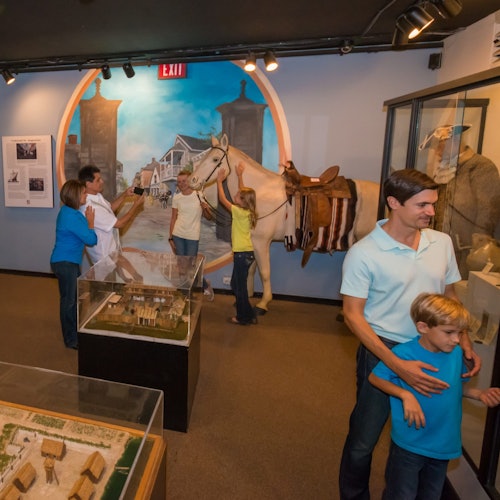 People exploring a museum exhibit featuring a life-sized horse model, historical displays, and architectural models.