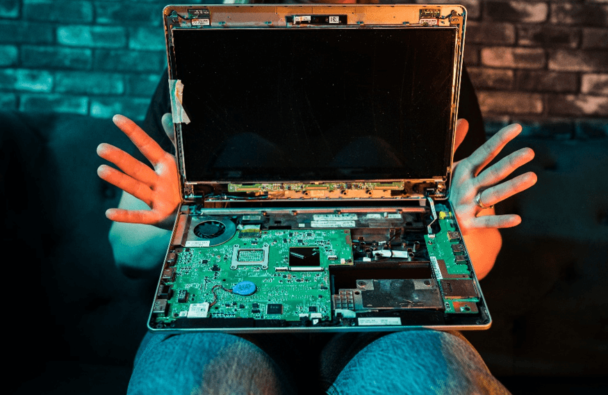 Person holding open laptop revealing its internal components. The screen is dark and the motherboard is visible