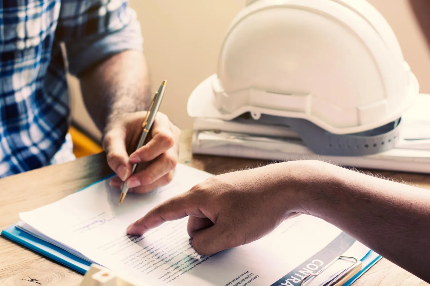 Profissionais analisam e assinam documentos técnicos, representando a preparação de evidência para pleitos em obras e contratos.