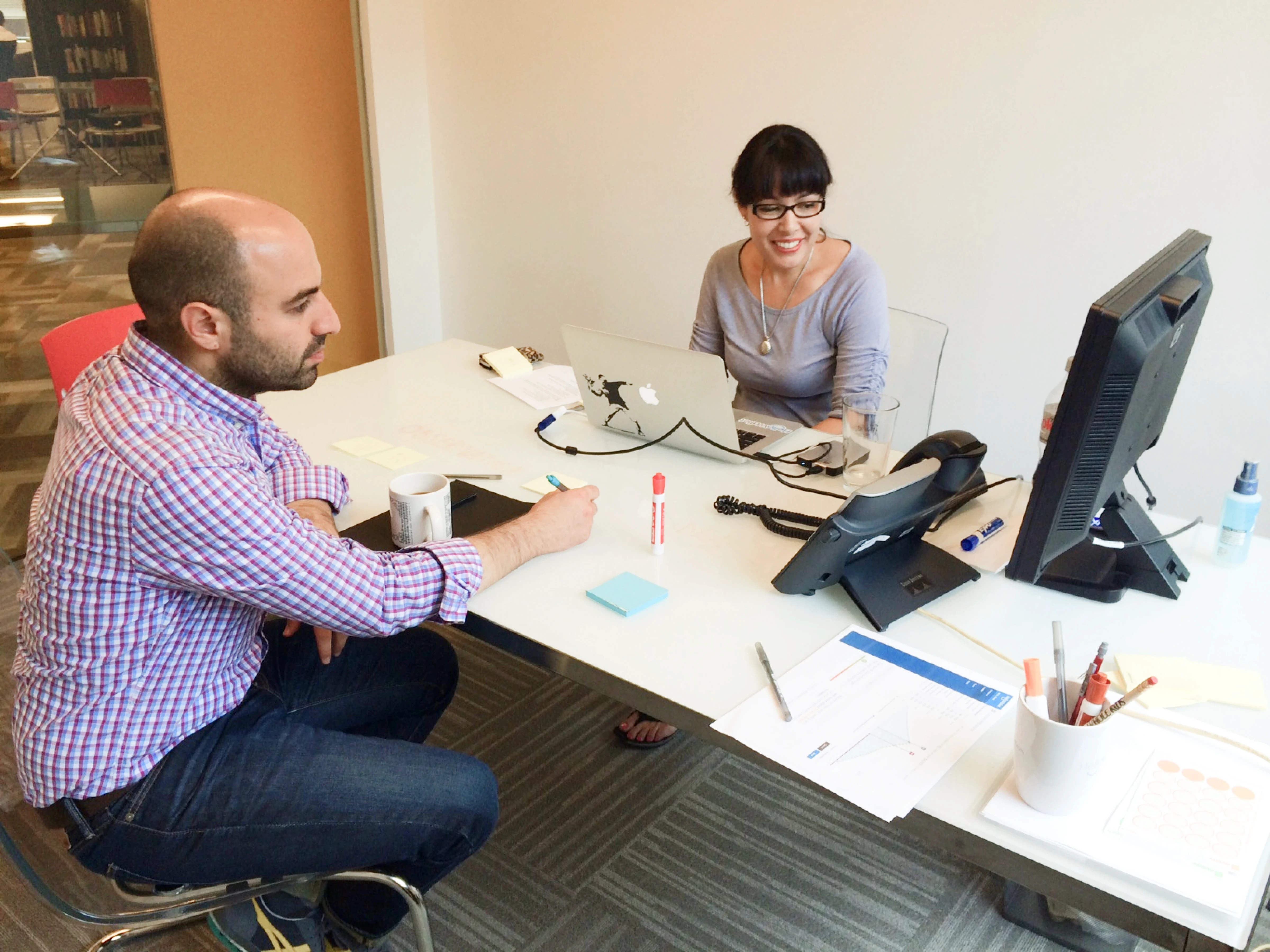 A product manager and researcher sitting at a desk, watching a remote session on a computer monitor.