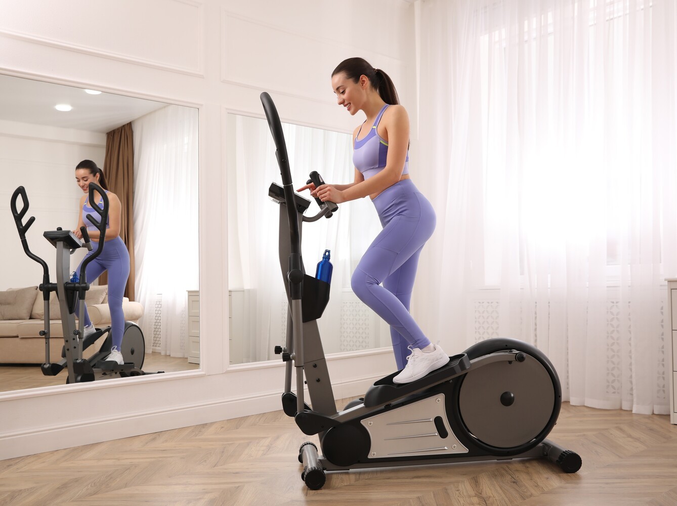 woman turning on and setting up her machine to do an elliptical workout for weight loss at home in her living room