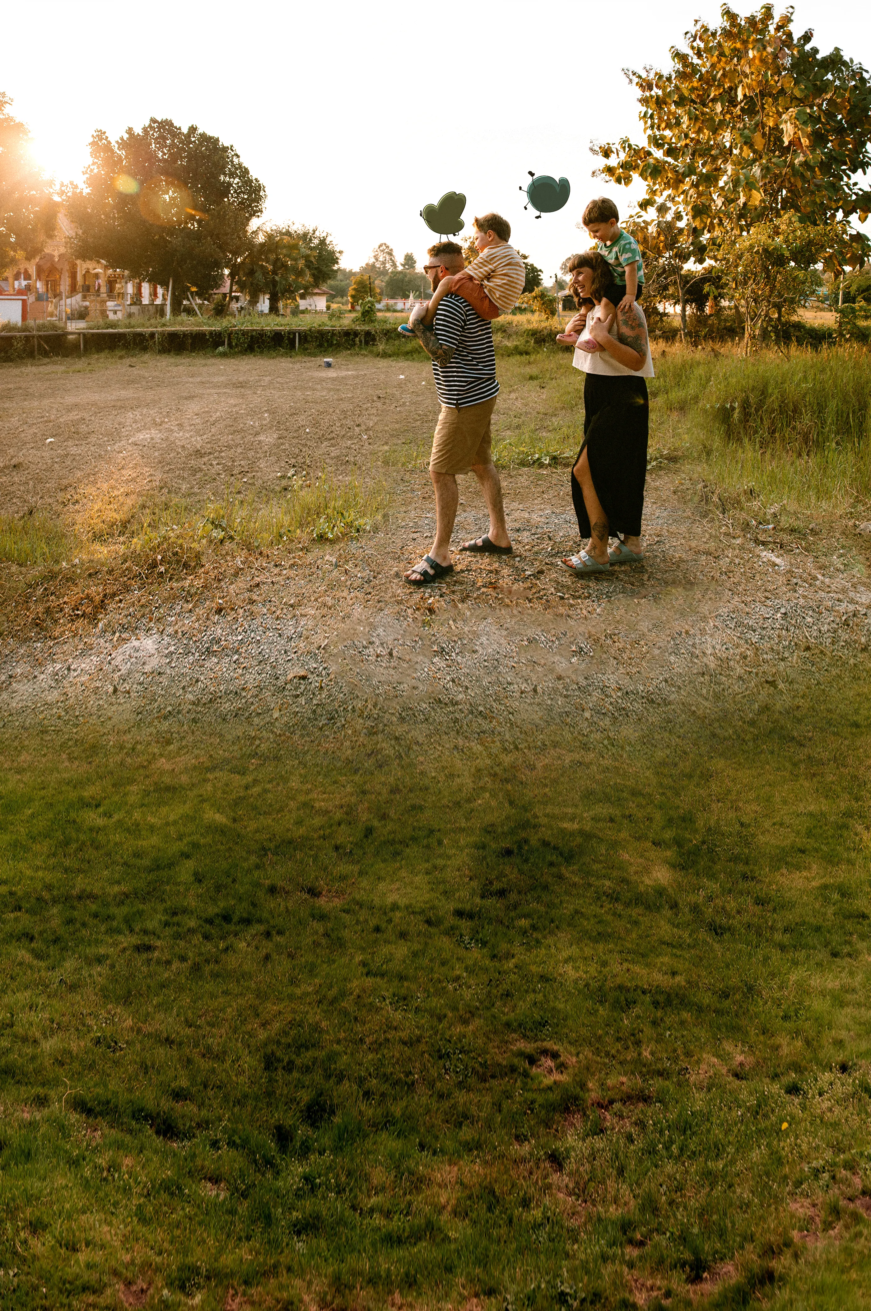Nick and Flo walking through a grassy field at sunset, each carrying their sons on their shoulders