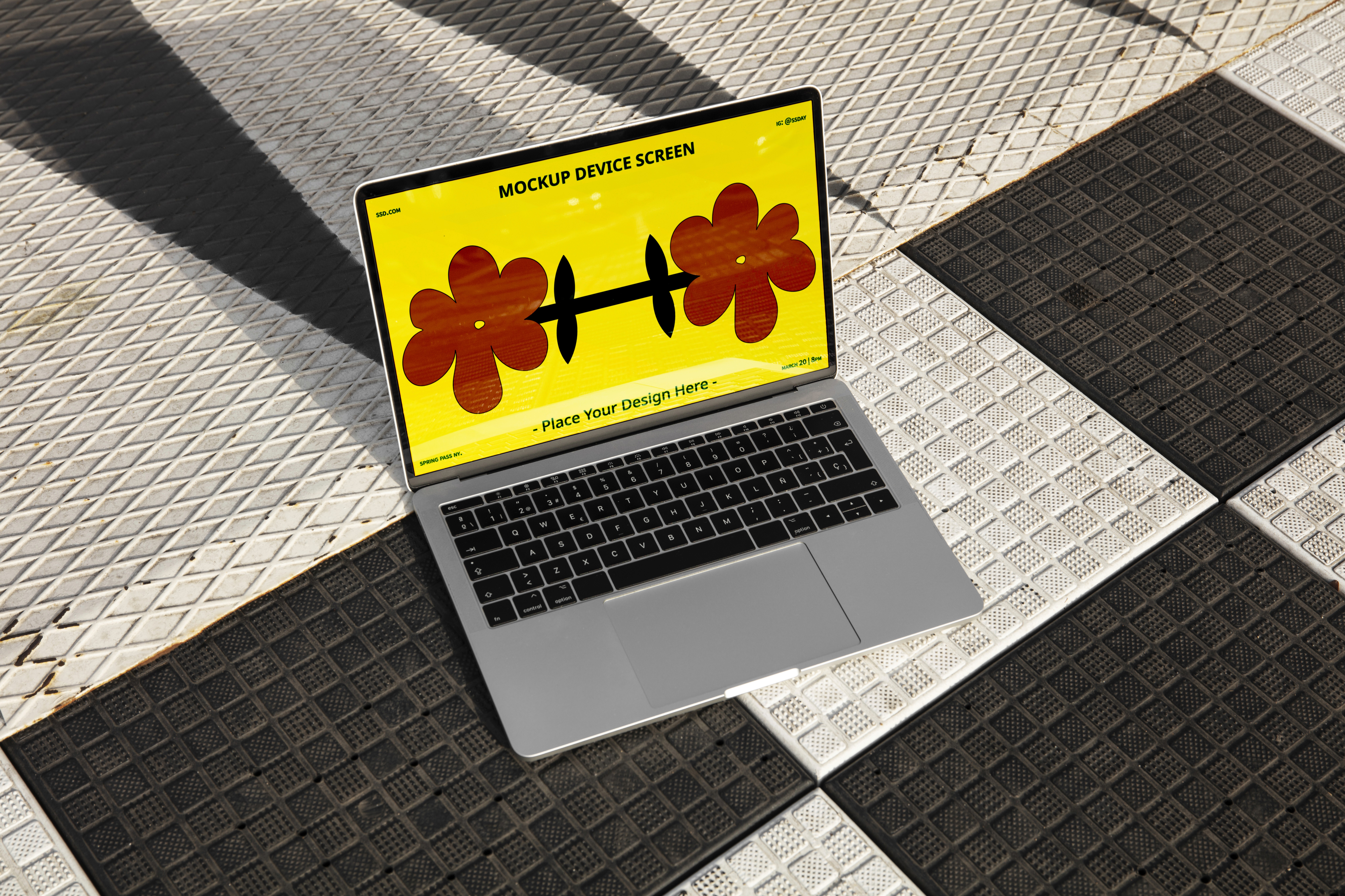 A silver laptop mockup sitting on a textured metal diamond plate surface, featuring a vibrant yellow screen with floral illustrations under natural sunlight.