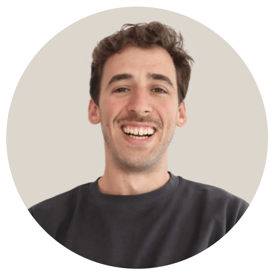 A smiling person with long, curly hair stands with arms crossed, in a modern, blurred background.