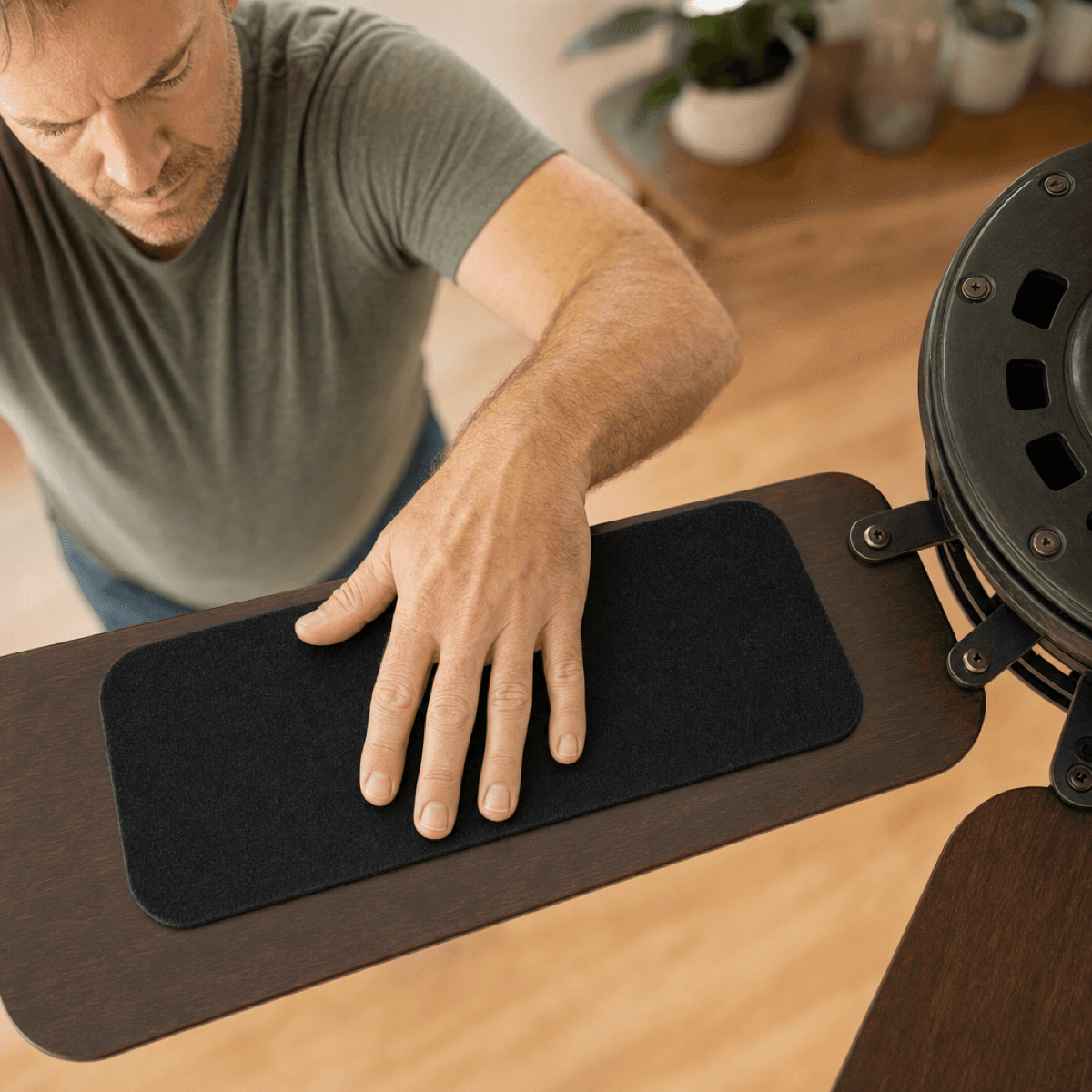 A hand pressing a jet-black rounded-rectangle carbon pad onto the top of a fan blade
