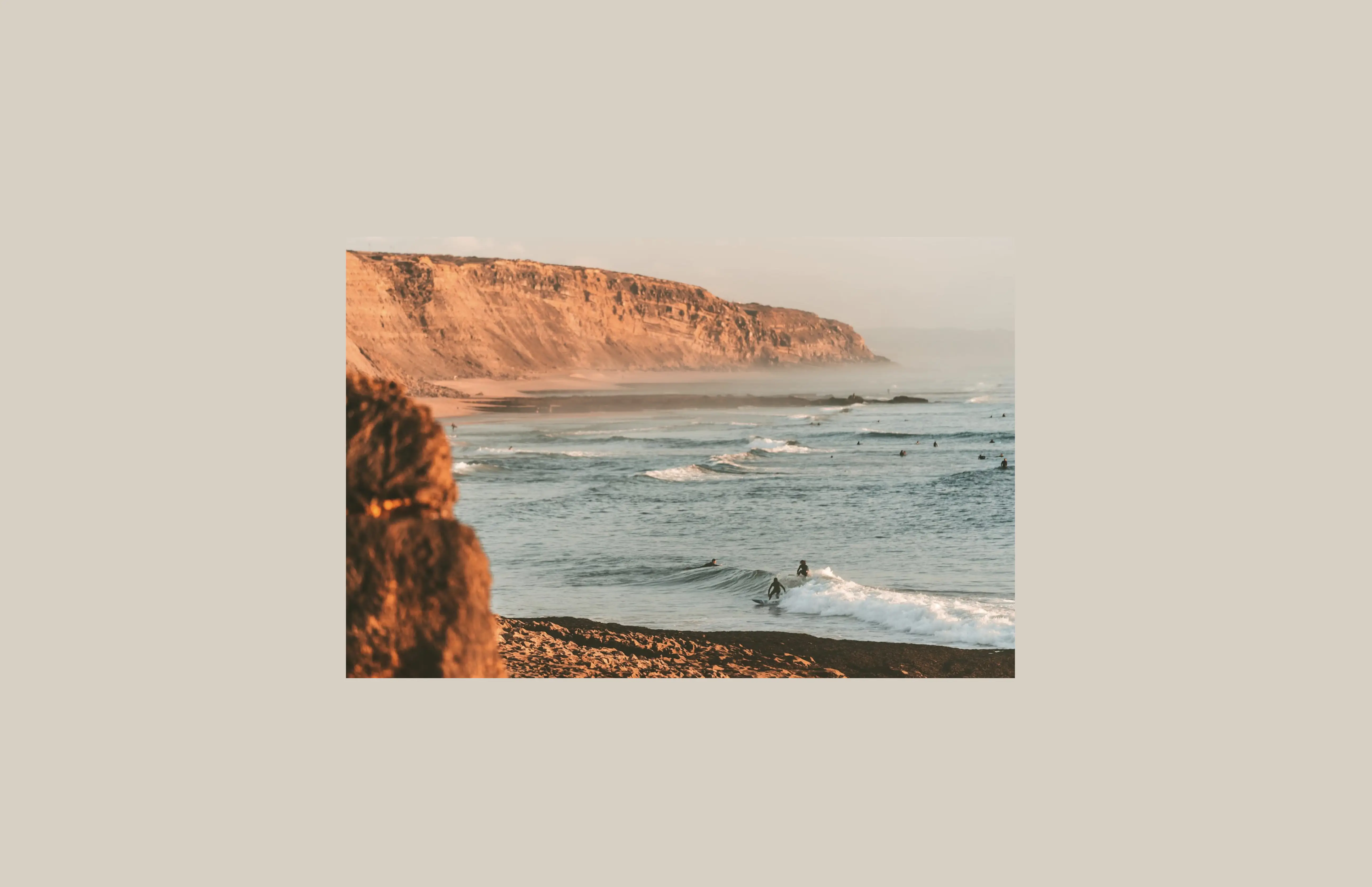 Surfers riding waves below dramatic cliffs at Taghazout Morocco — 102,974 satoshis for a full beginner surf day, ranked fifth globally in the Bitcoin Weight surf audit 2026.