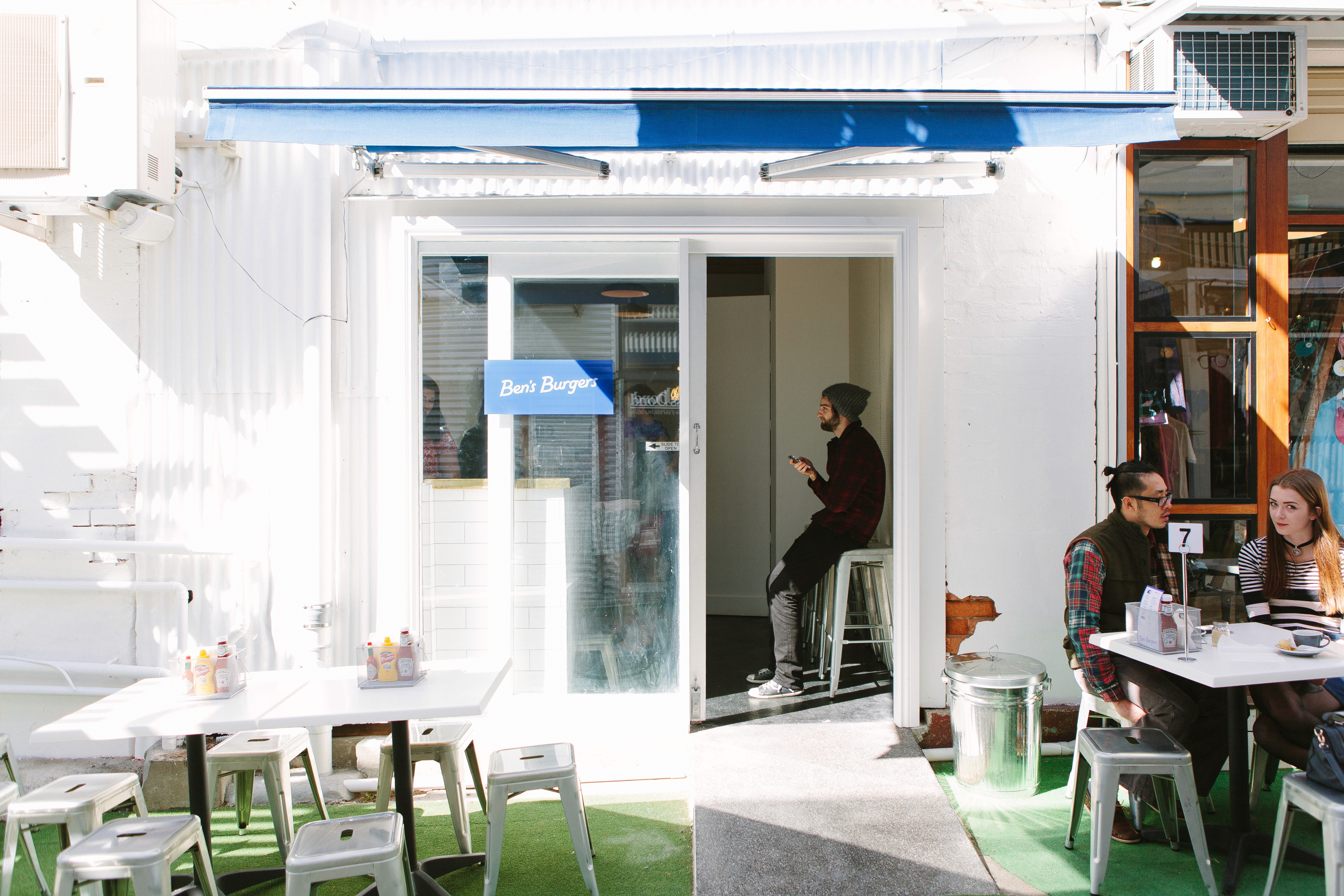 Ben’s Burgers laneway frontage with outdoor seating, customers dining, and the small white kiosk opening directly onto Winn Lane.