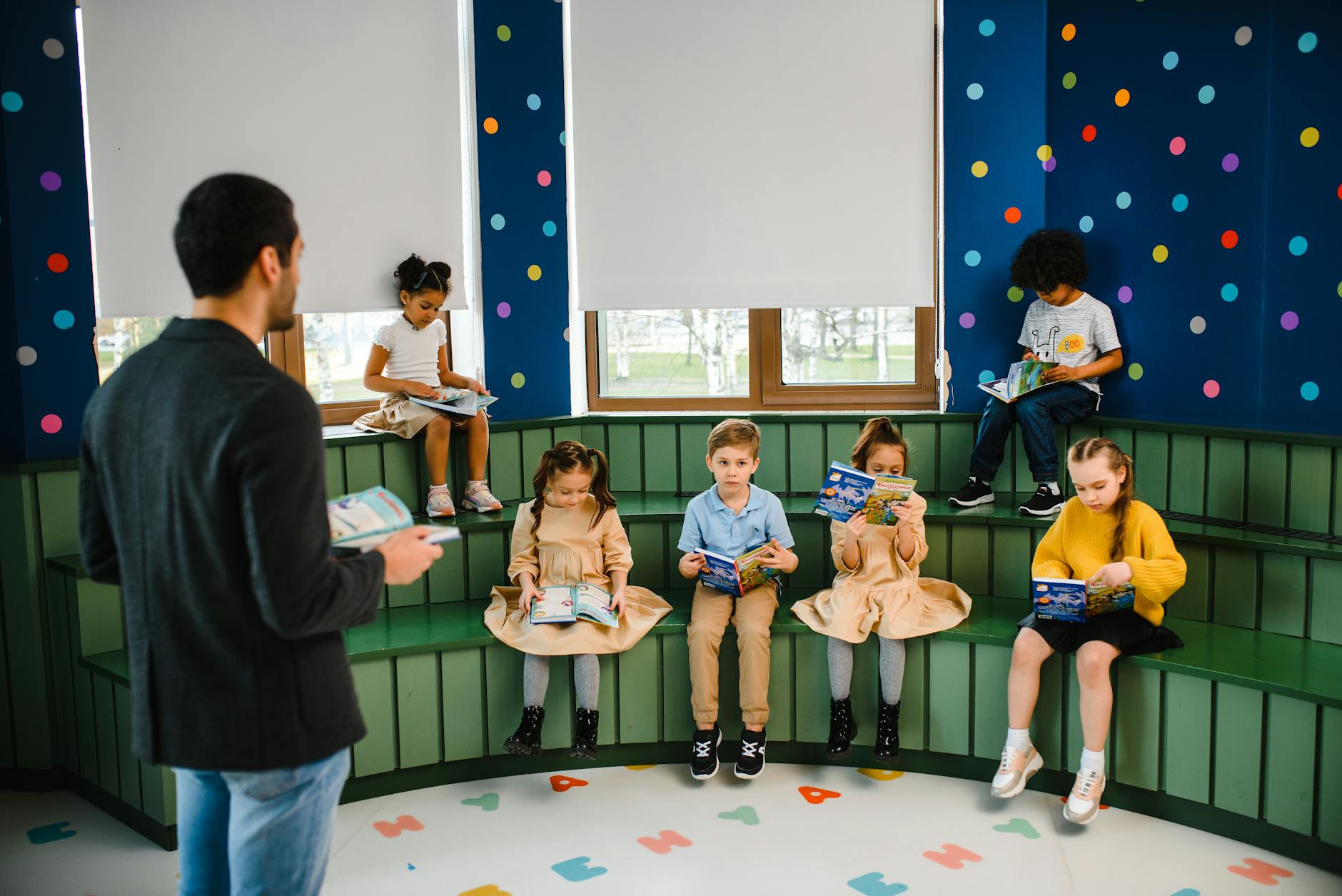 First grade students sit in a circle on the floor, each holding a different phonics reading books title.