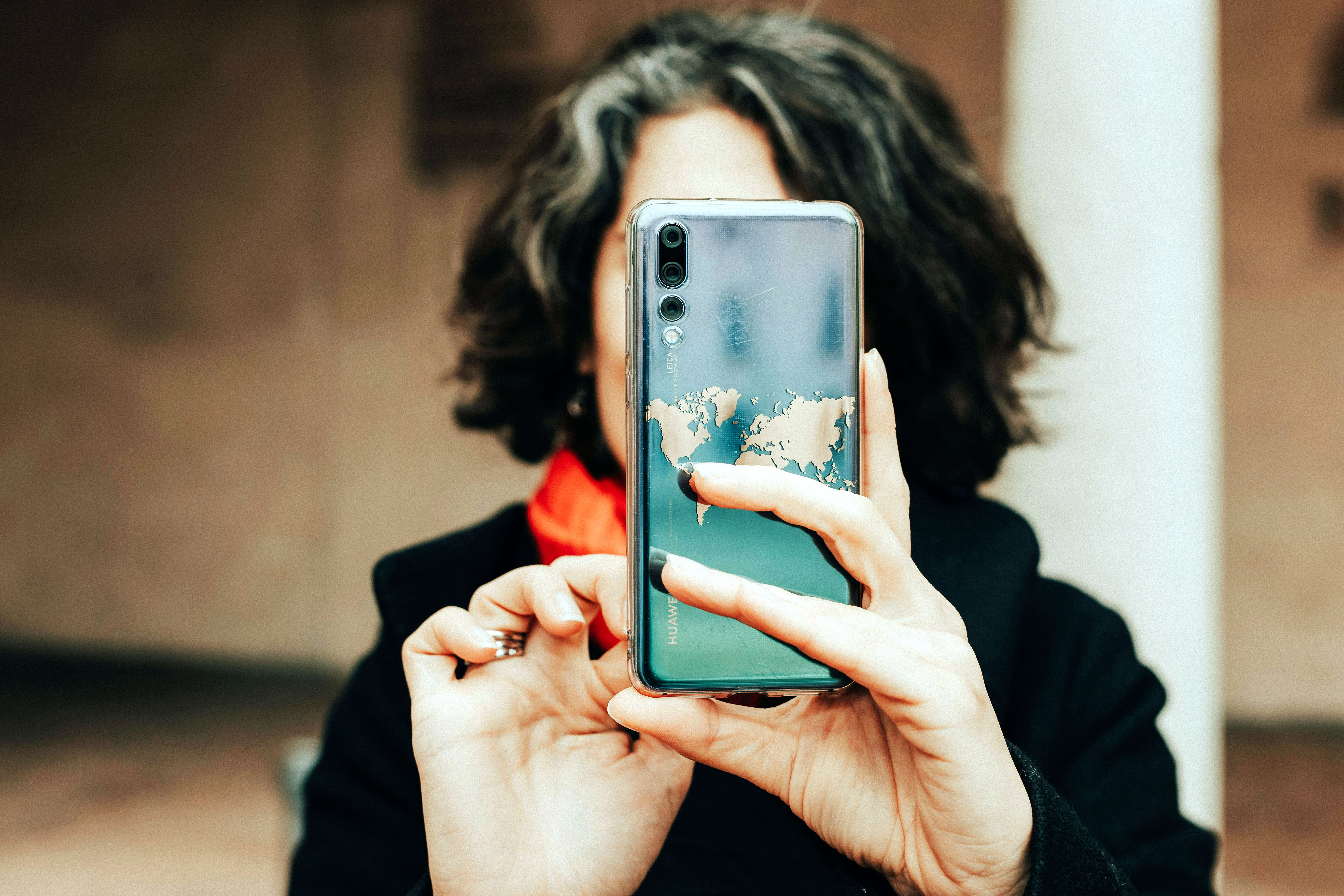 A person with curly hair holds a smartphone in front of their face, capturing a picture.