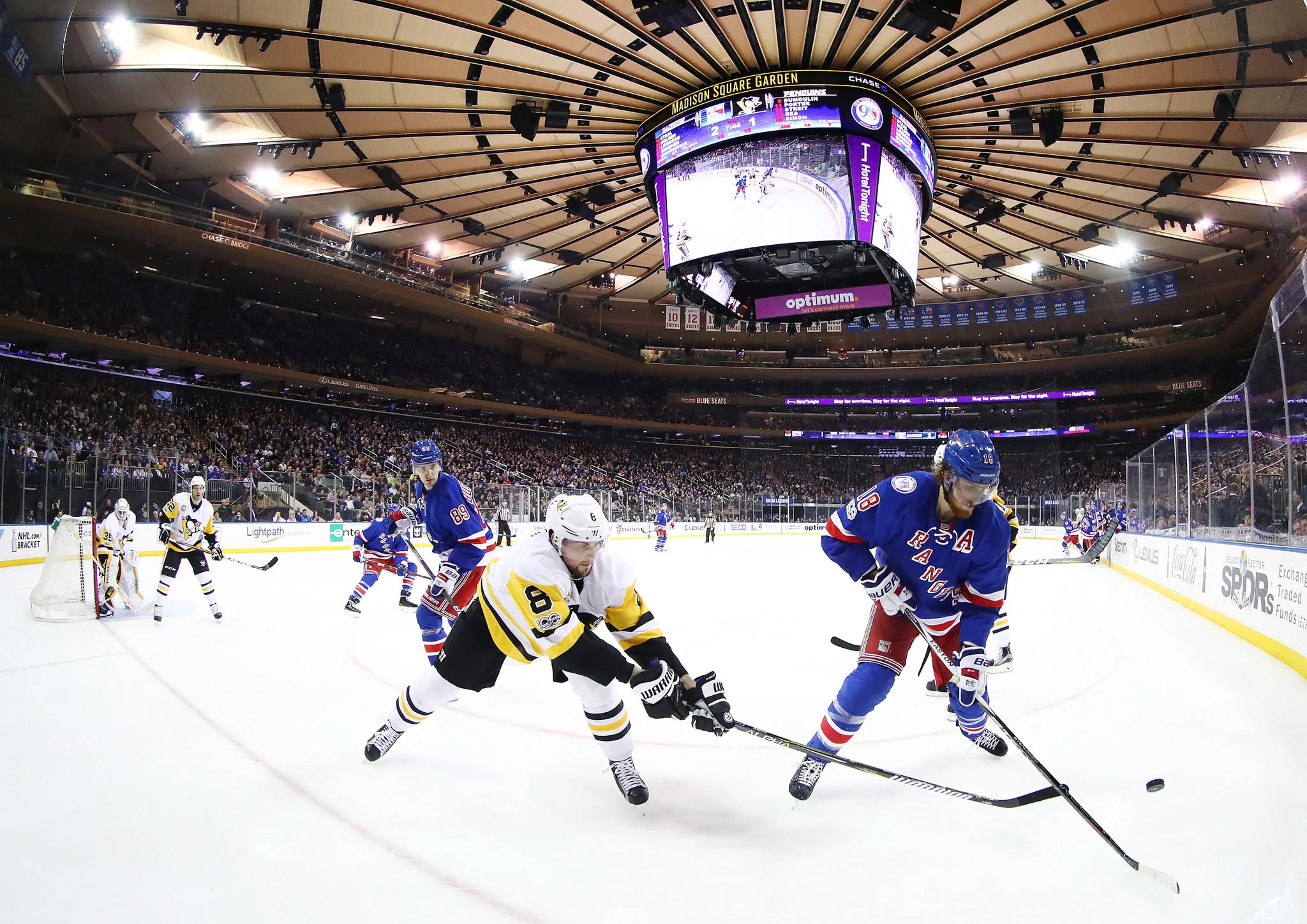 New York Rangers and Pittsburgh Penguins face off on the ice during an NHL game at Madison Square Garden with a packed crowd in the arena.
