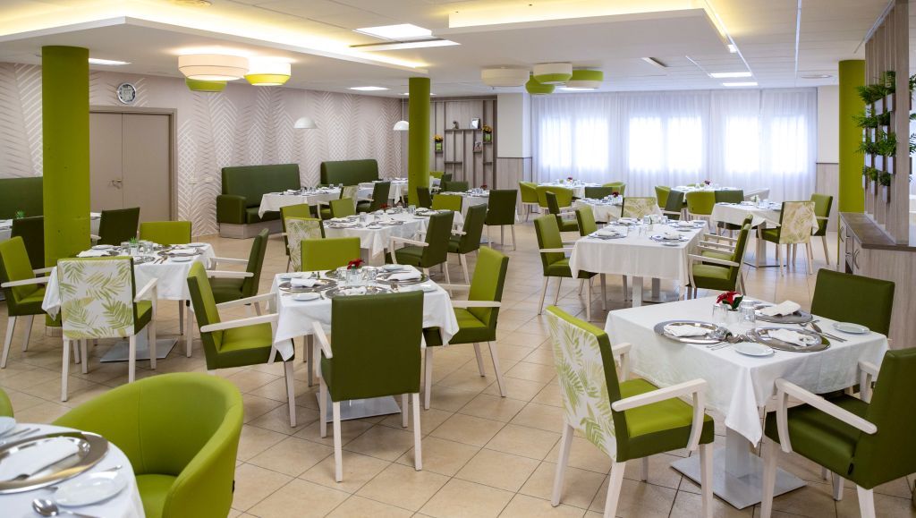 Large dining room with green chairs, white tablecloths, and decorative green columns.