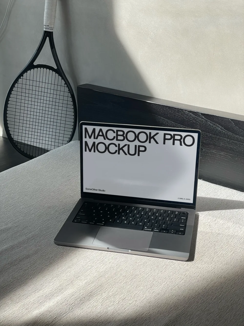 A MacBook Pro mockup placed on a textured light gray surface, with a black tennis racket leaning against a wall in the background. Soft natural light casts shadows, creating a minimalist aesthetic.