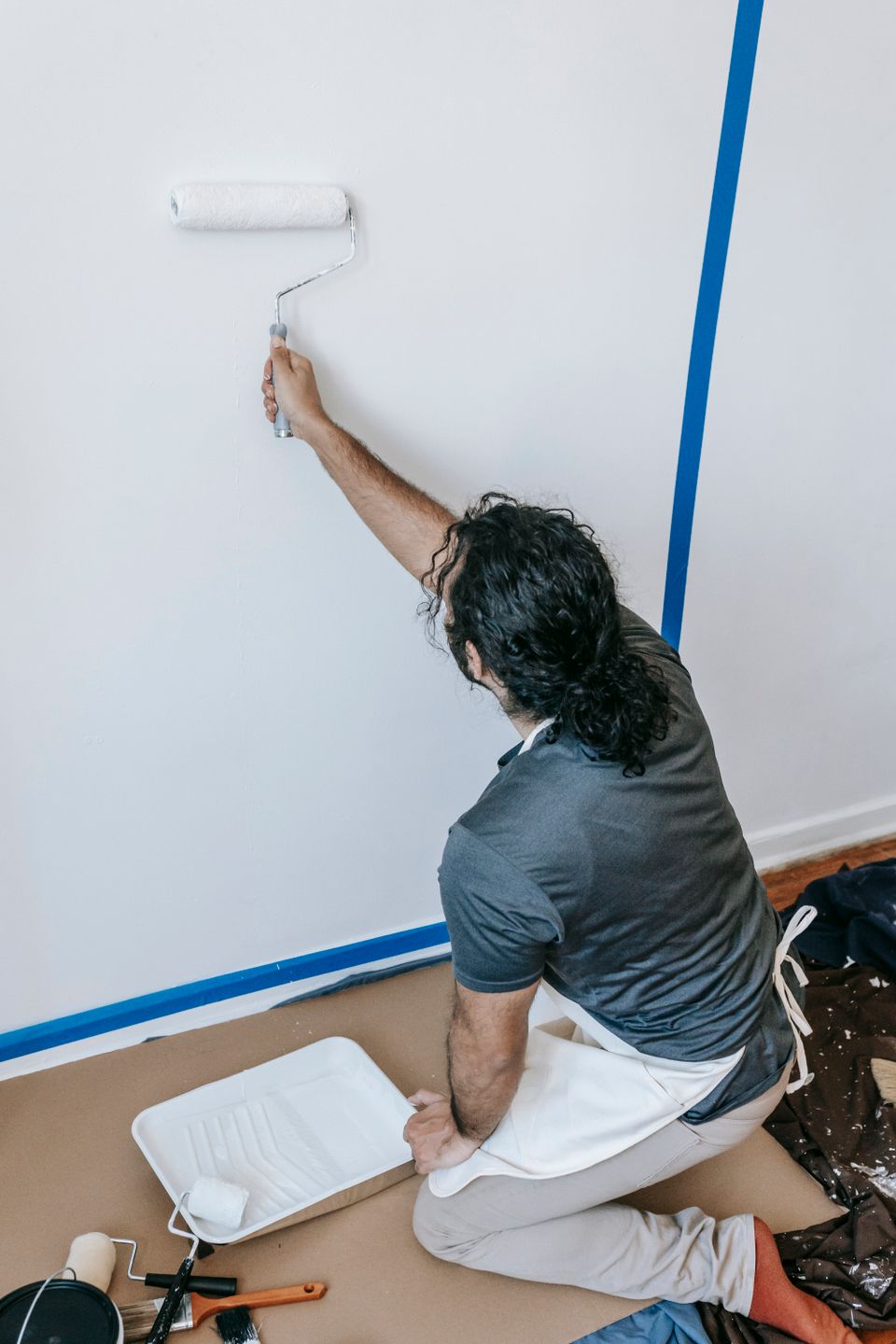 Un peintre repeint un mur au rouleau, avec les contours protégés par du ruban bleu.