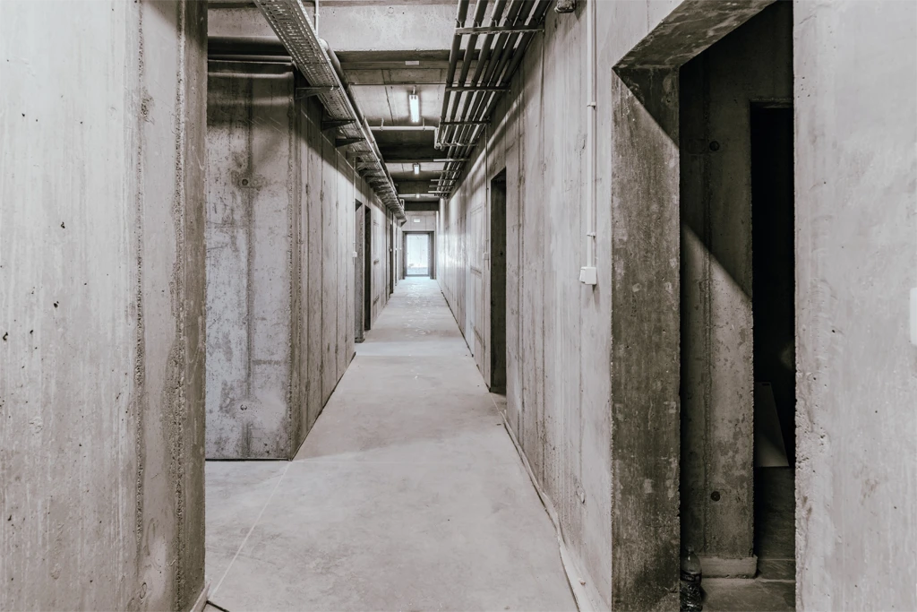 Korytarz z betonowymi ścianami i drzwiami po obu stronach. Widok z perspektywy w głąb korytarza.