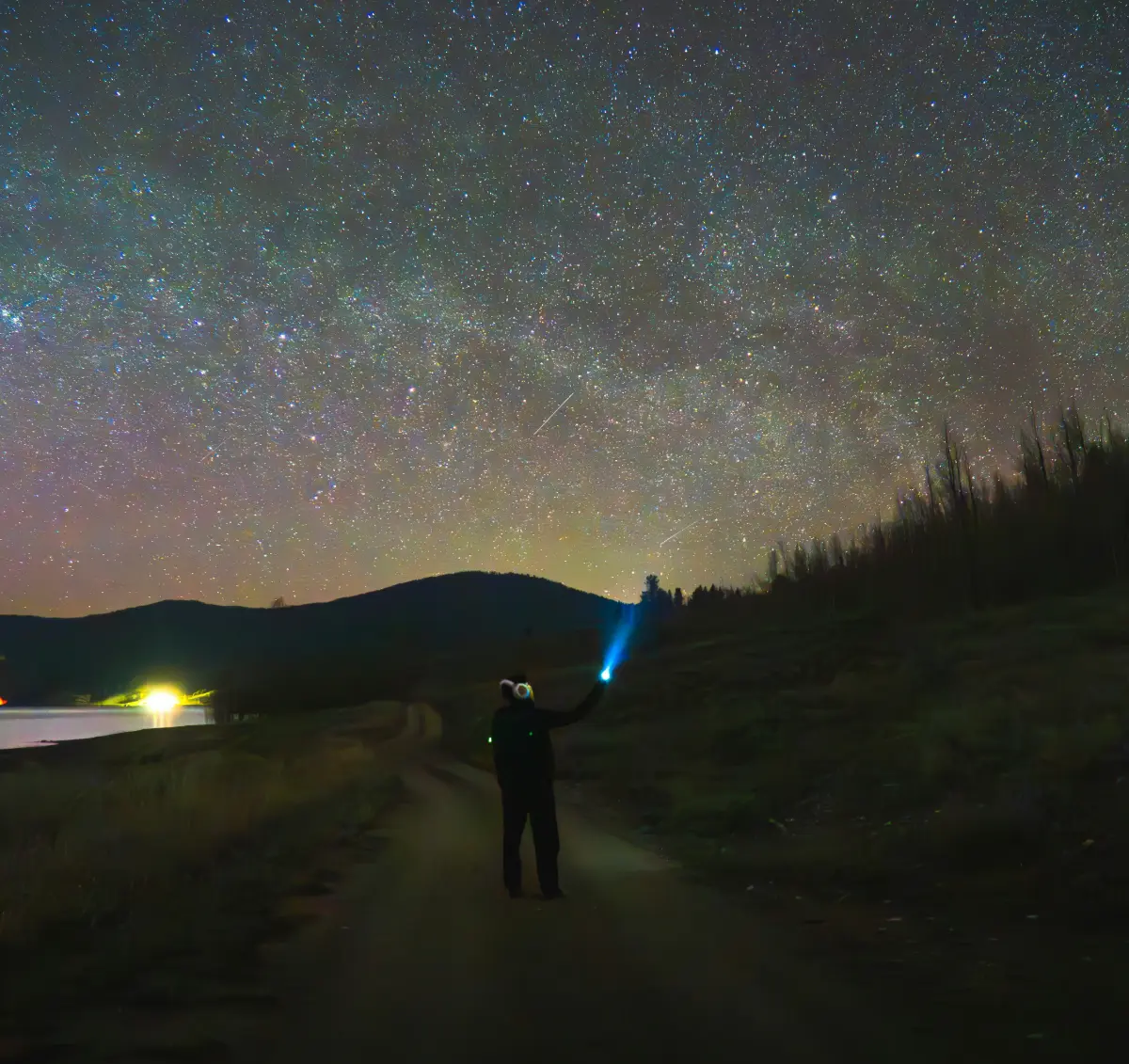 Person with flashlight under a vibrant starry night sky.