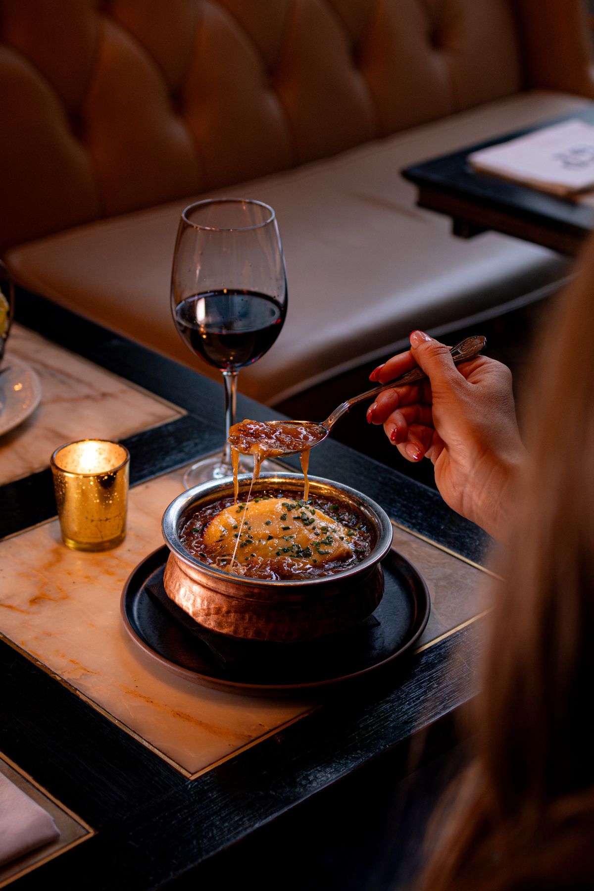 French onion soup enriched with Indian aromatics, topped with melted cheese and paired with red wine in a modern fine dining setting.