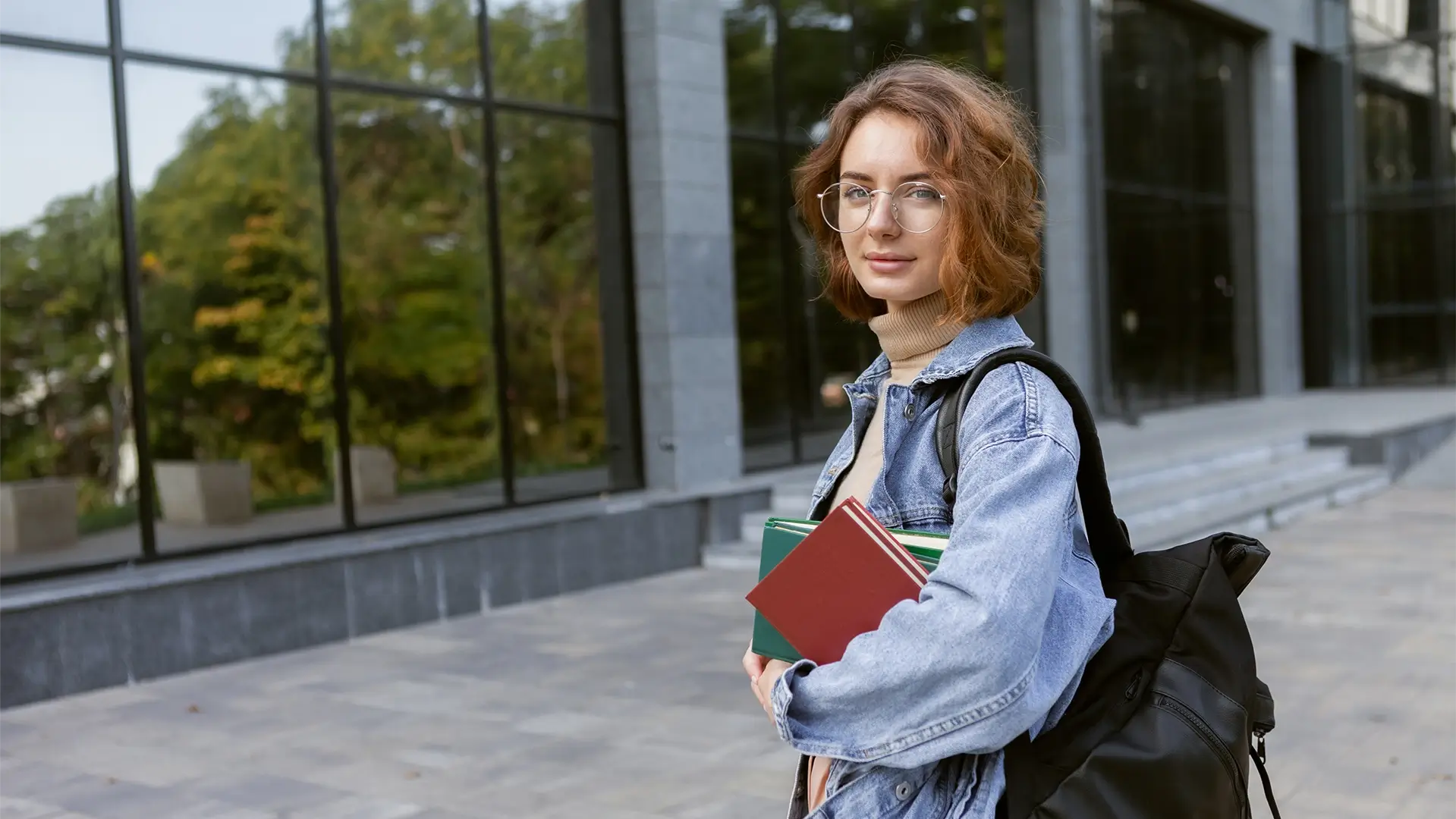 Studentka s knihami před univerzitní budovou. Spoluprací se školami dáváme prostor talentům růst.