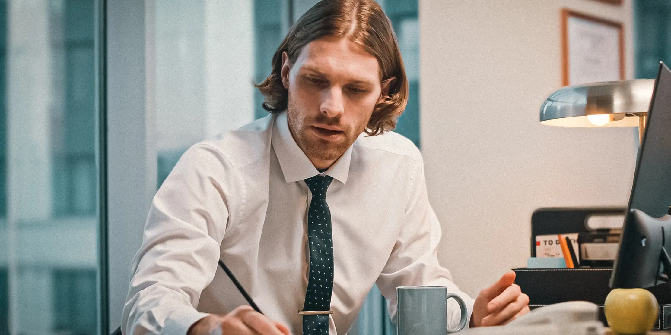 Professional in a white dress shirt and polka dot tie working at a desk with a coffee mug and apple nearby