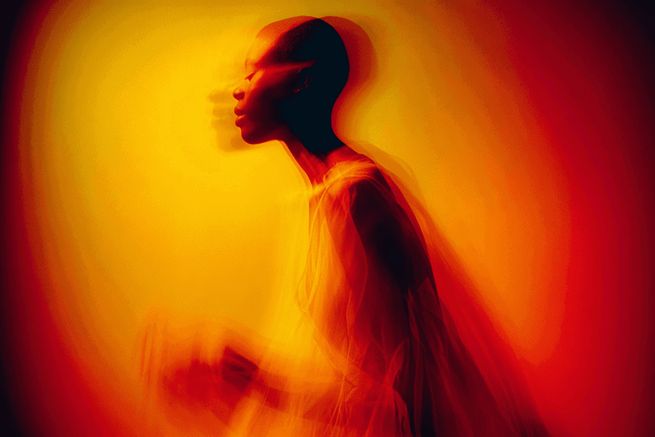A blurred silhouette of a person against an orange and yellow background, creating an ethereal atmosphere.