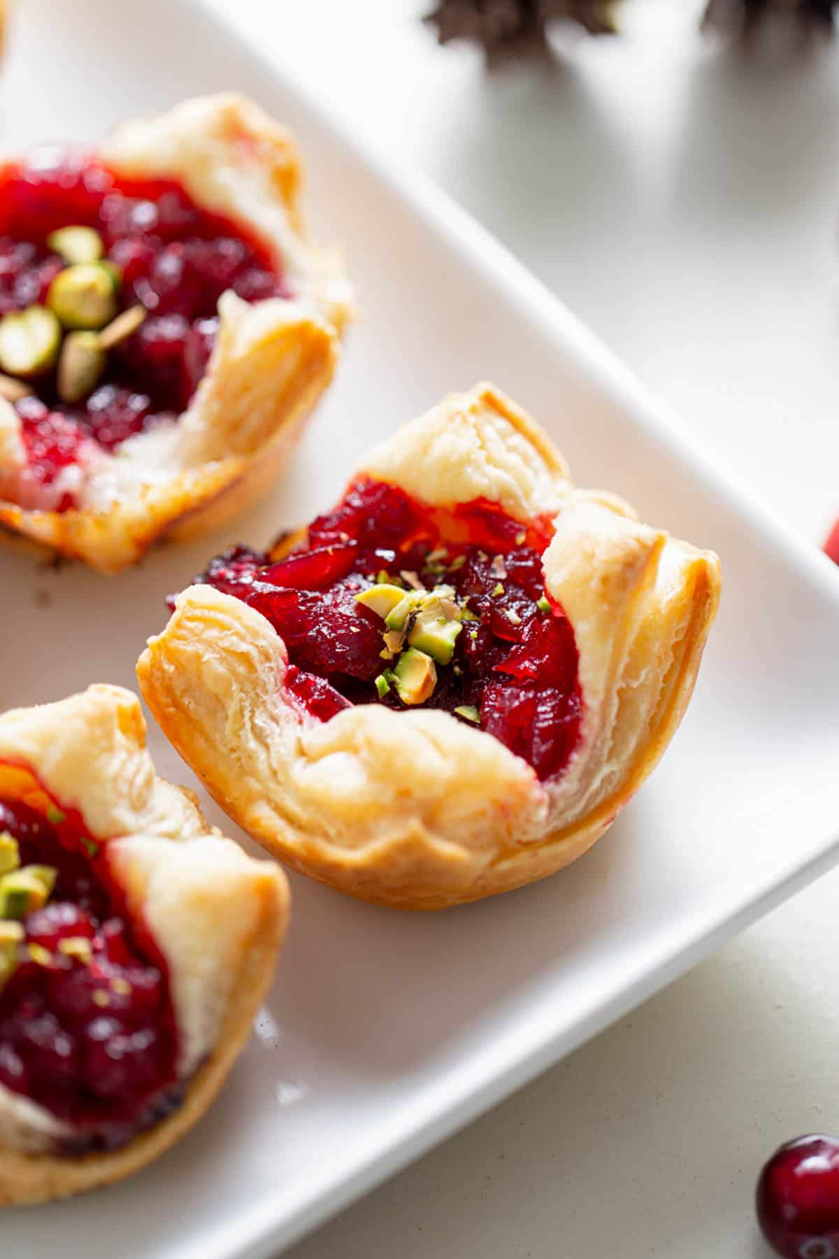 A tray of golden-brown cranberry brie bites, featuring flaky pastry cups filled with creamy brie cheese and topped with a vibrant cranberry sauce and nuts.