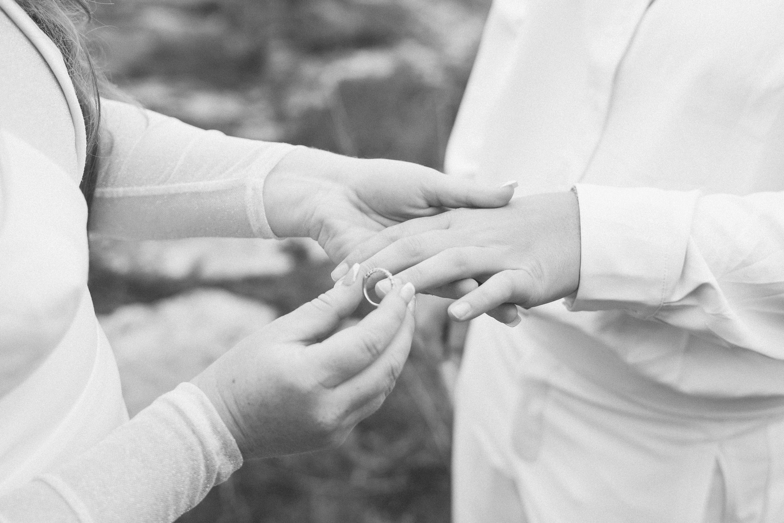 Monochrome close-up of one partner placing a ring onto the other's hand.