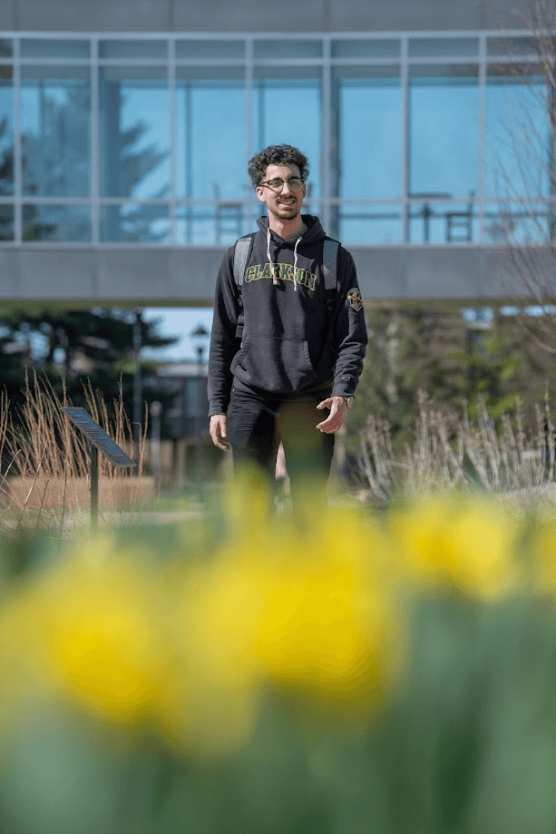 Vertical portrait of Frank at Clarkson University with blurred yellow flowers in the foreground
