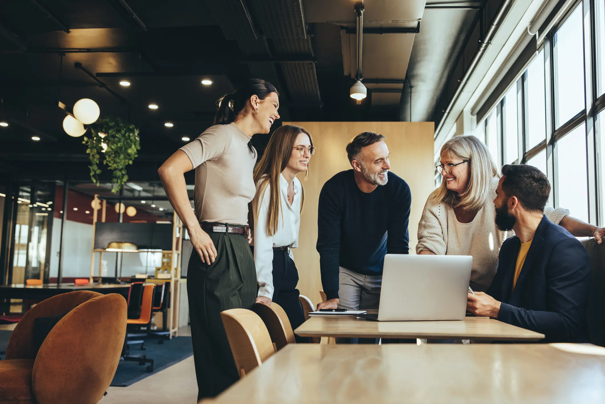 Mixed-age professional team collaborating around a laptop in a modern office representing high performance teaming