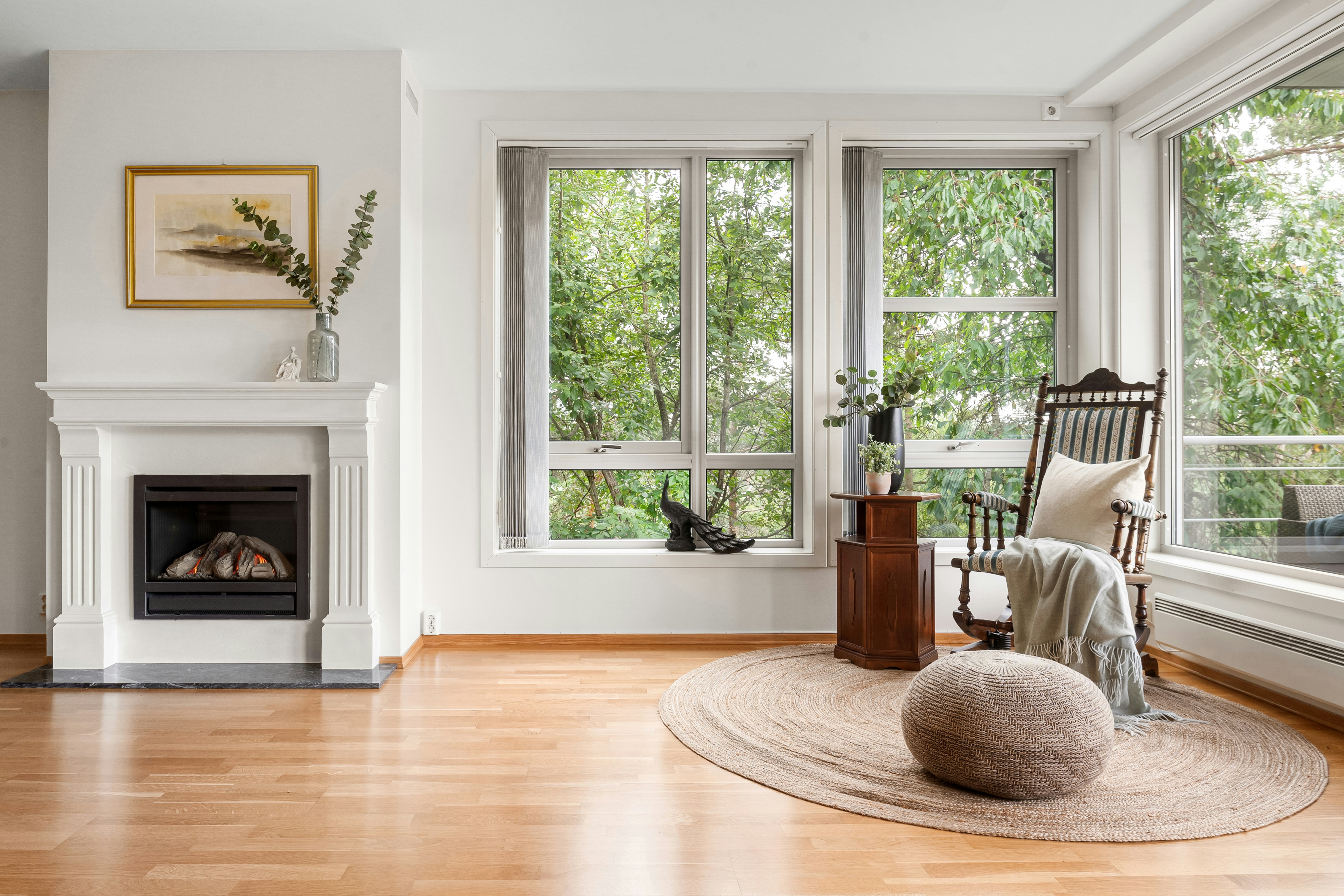 Bright Scandinavian sitting room with white fireplace, antique rocking chair, and treetop views