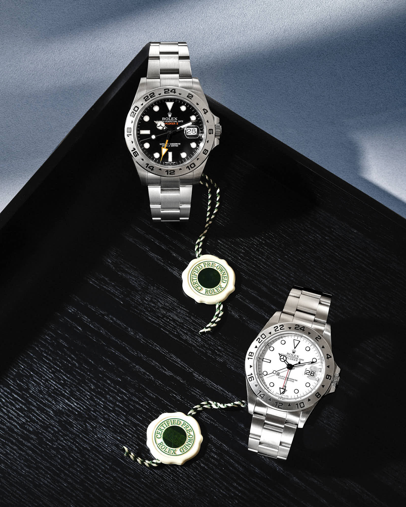 Luxury Rolex Explorer II watches with silver bracelets on black wood background.