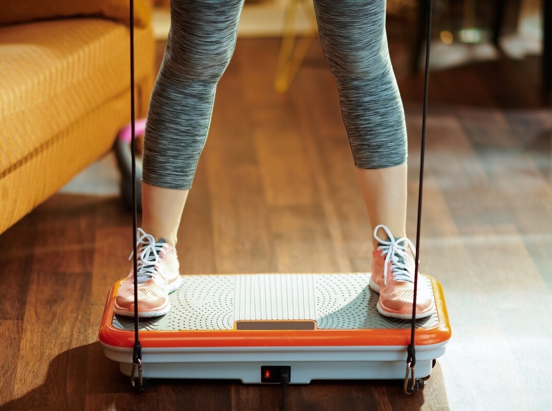 woman in fitness gear using a vibration plate for weight loss at home in her living room