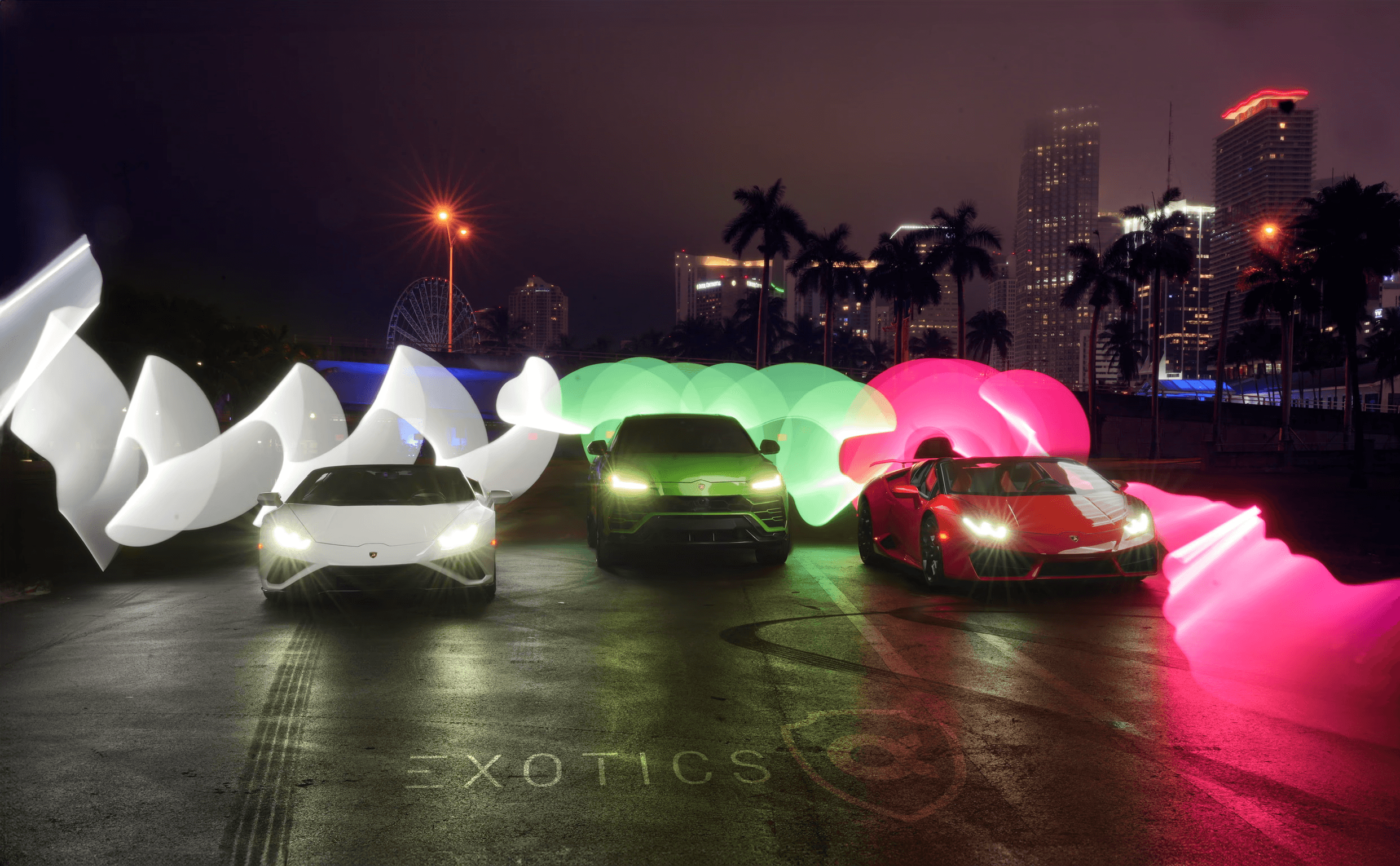 Two people in a workshop, one standing and smiling while the other leans over a car, working on it.