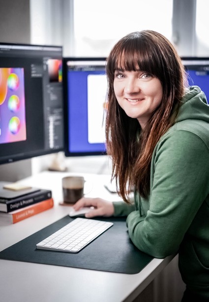 Natalia Opielka przy biurku z monitorem i tabletem graficznym.