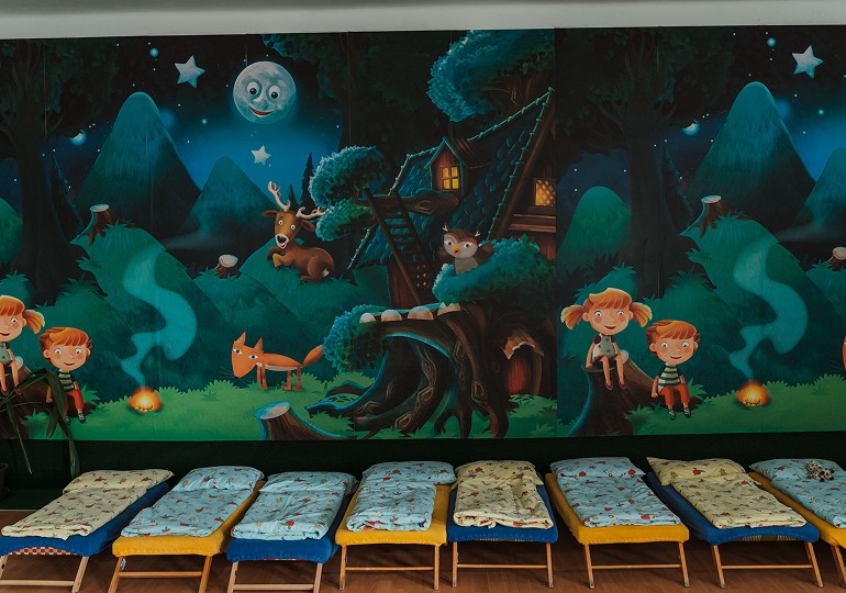 Ložnice ve školce s postýlkami a nástěnnou malbou lesa