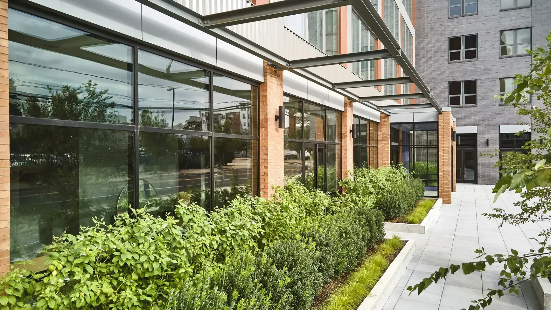 A modern building with large windows overlooking a landscaped area featuring greenery and a pathway.