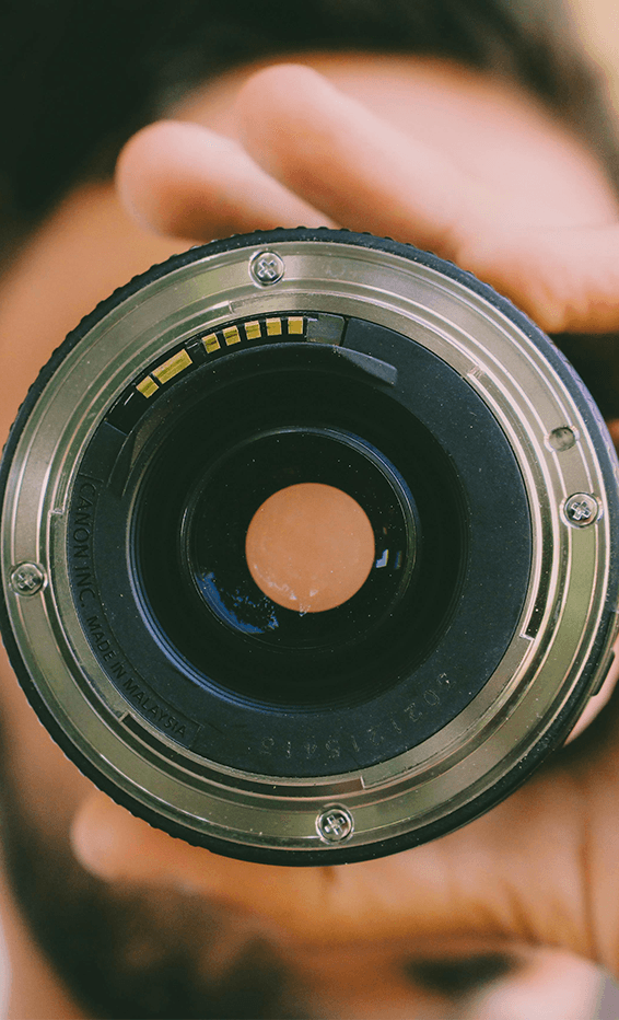 Close-up portrait of a person wearing a gray insulated hooded jacket with the hood up, showing their face framed by the hood against a light background.