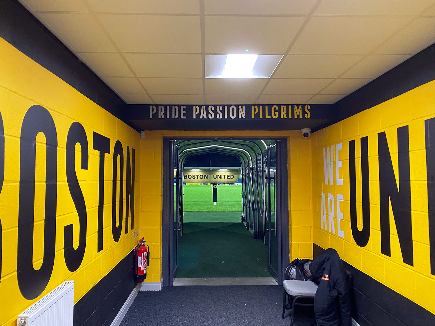 A view down the tunnel at Boston United's football ground. The football pitch is visible at the end of the tunnel