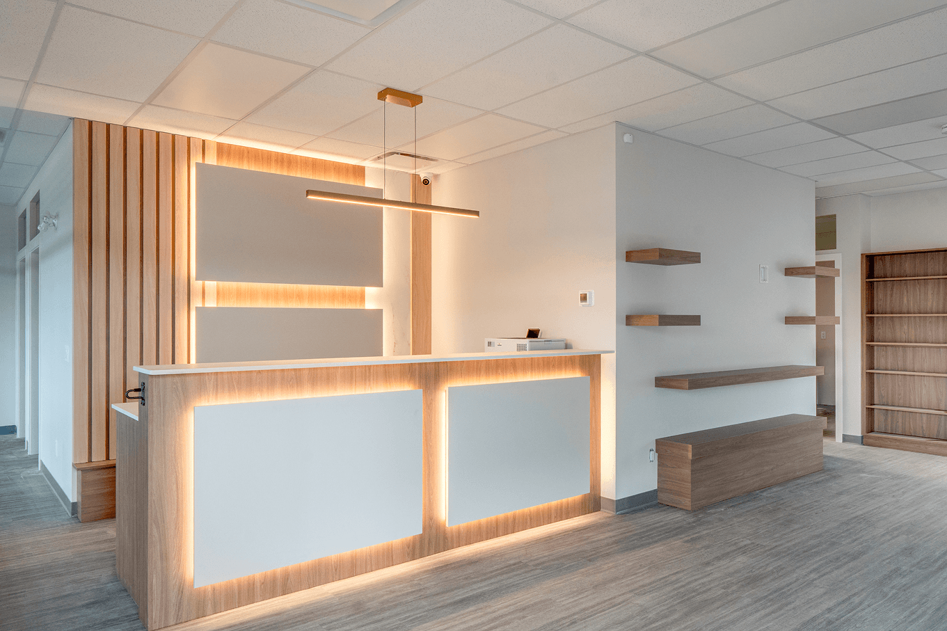 Wide view of custom-built reception area with illuminated millwork, wood slats, and open shelving.