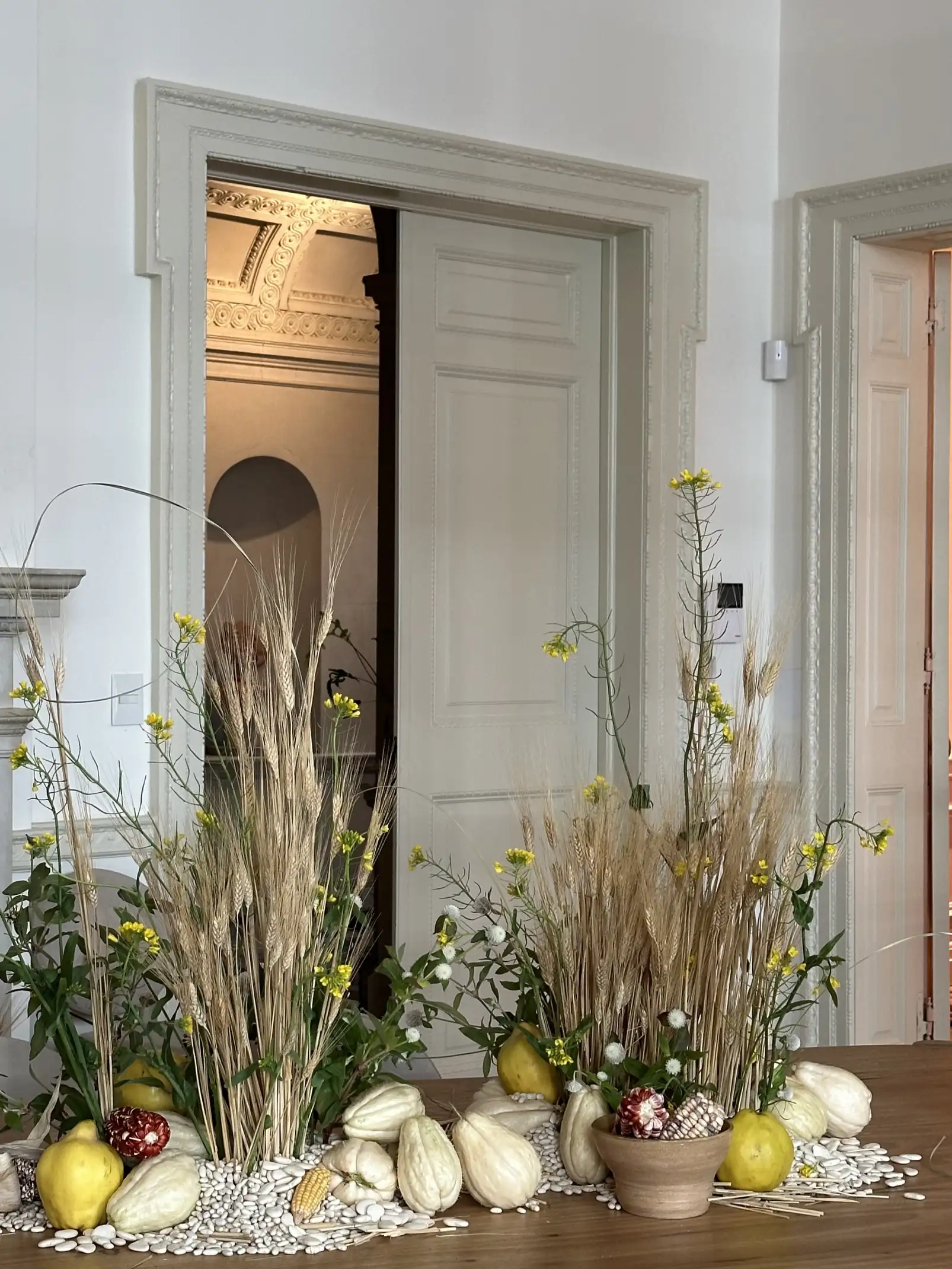 Arreglo decorativo con espigas, flores silvestres y calabazas sobre piso de madera para espacio interior clásico.