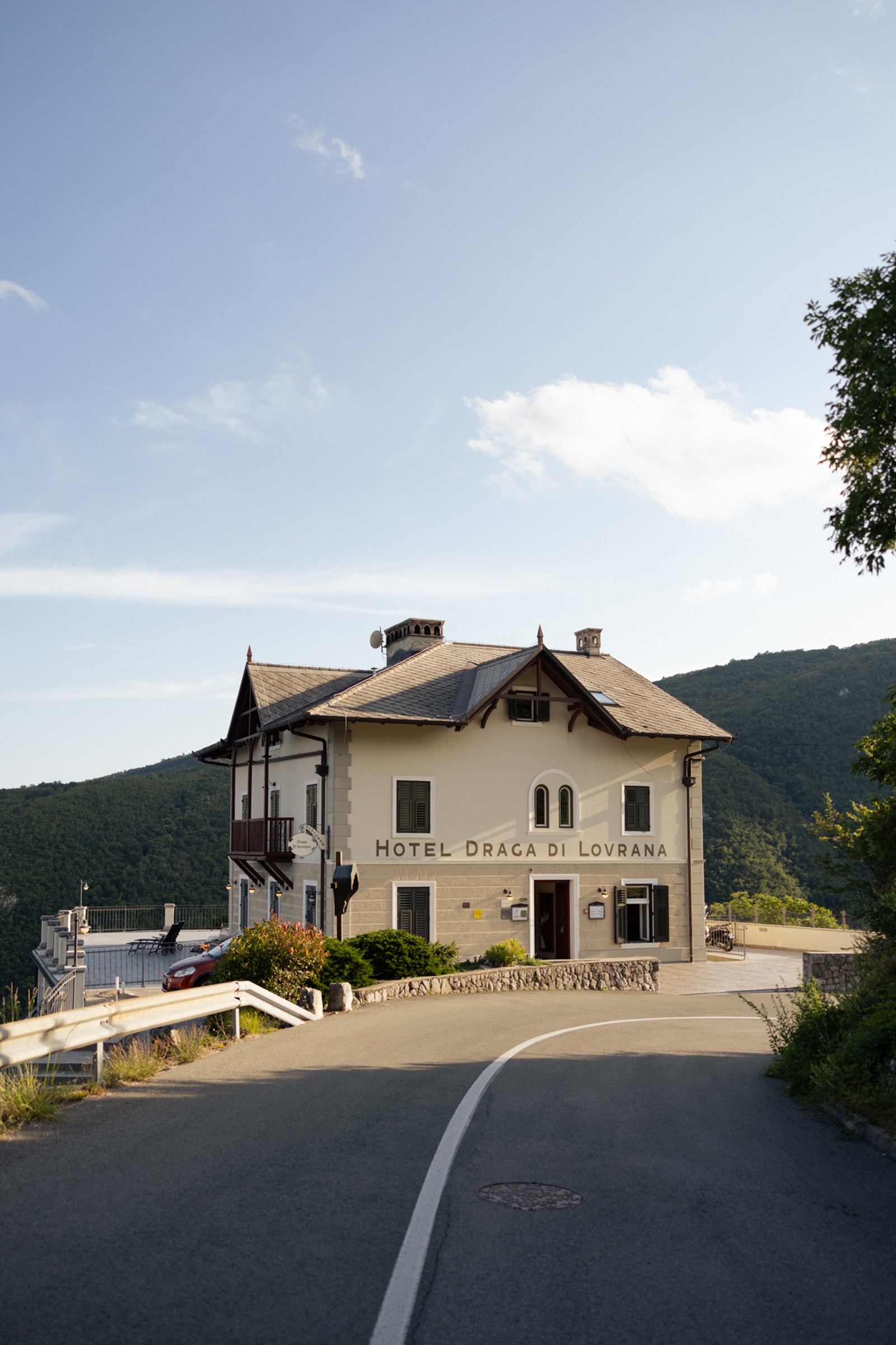 Austrian-style hotel sitting on the hillside with a forest behind and a road in the foreground