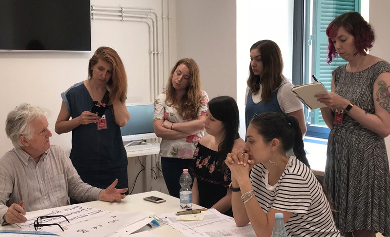 A photo showing students looking at a teacher that is explaining how to draw text letters.