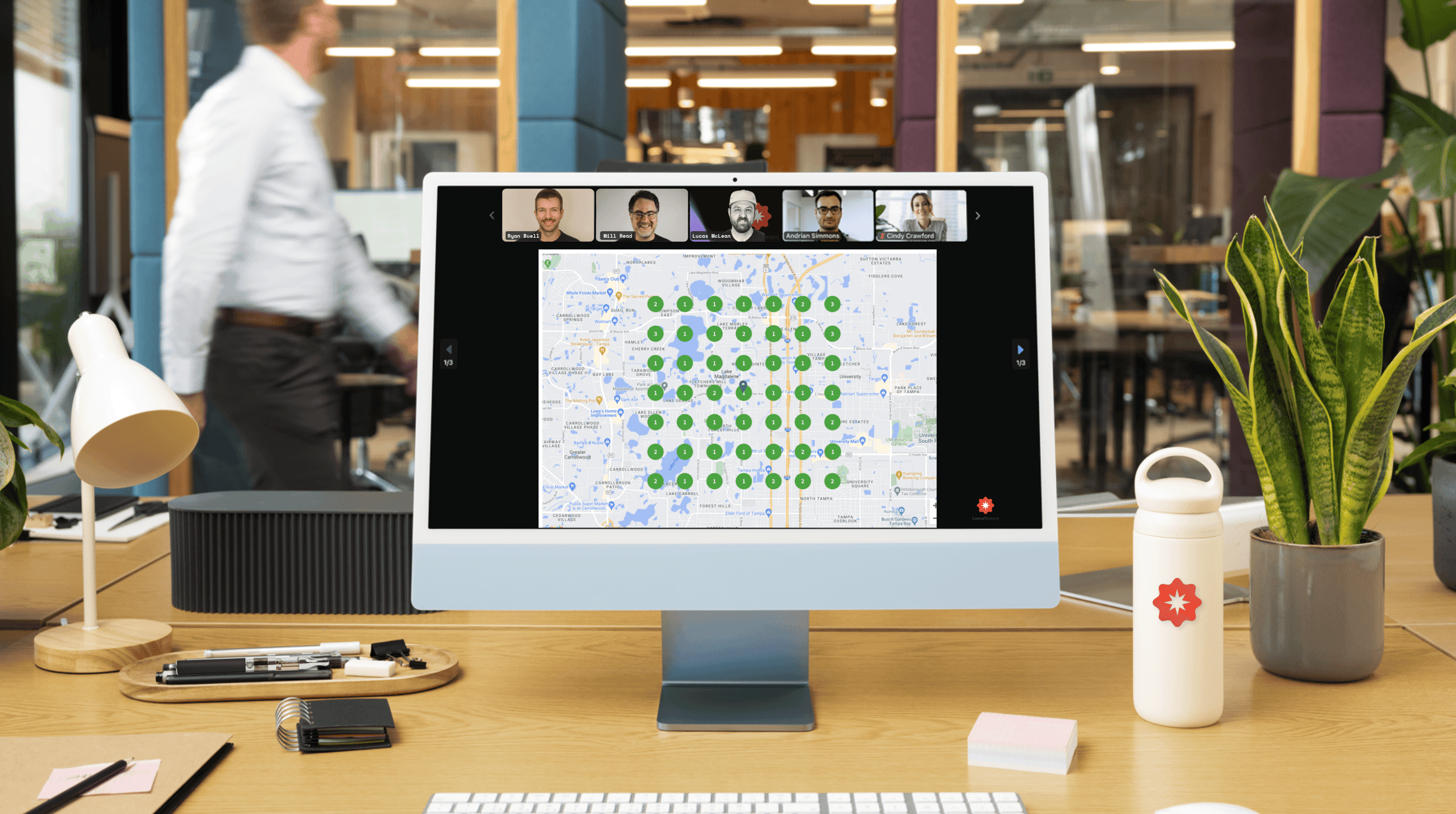 A computer monitor displays a map, with a person in the background in a modern office setting.