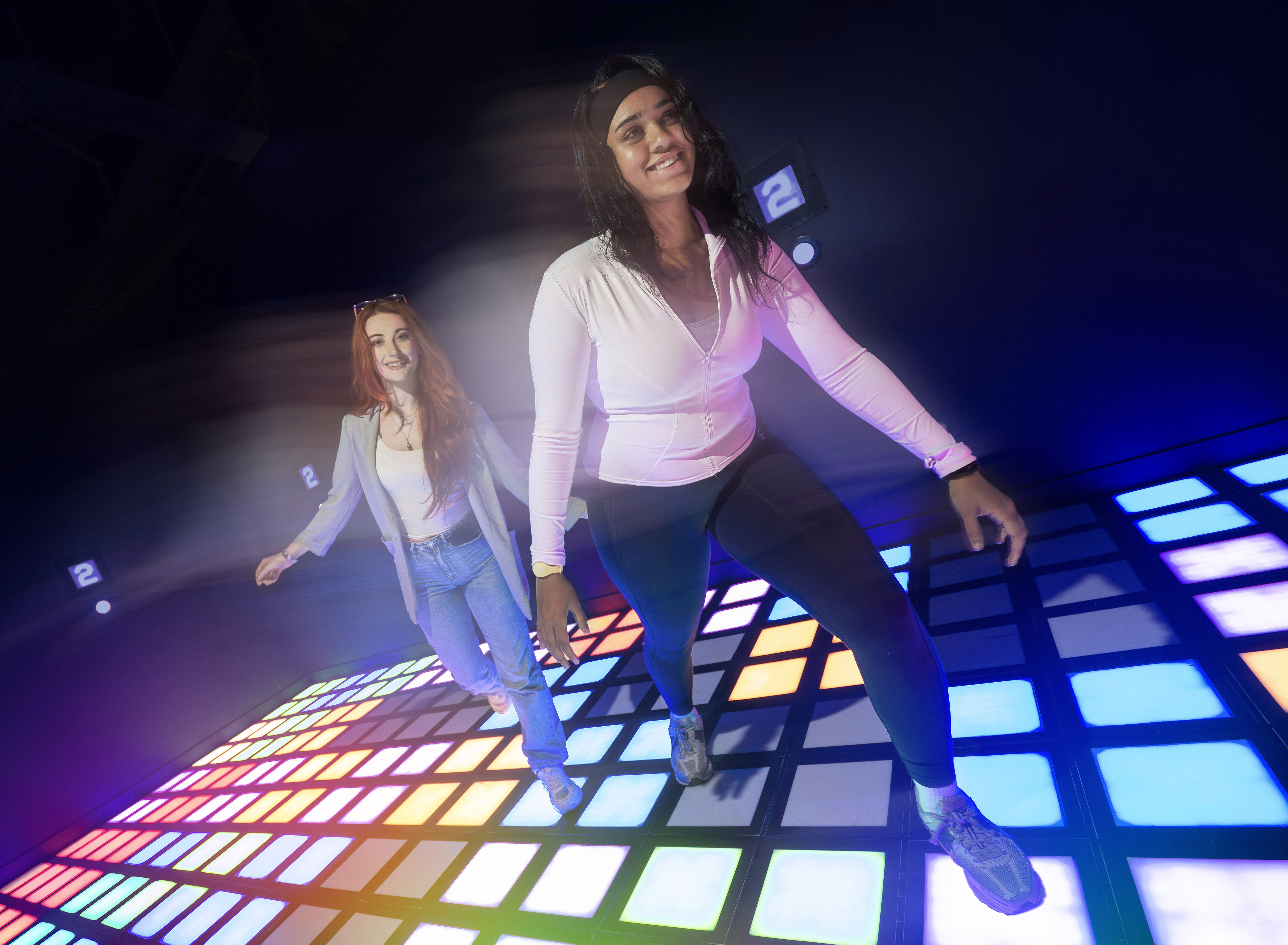 Two young women enjoy a colorful, interactive light-up dance floor.