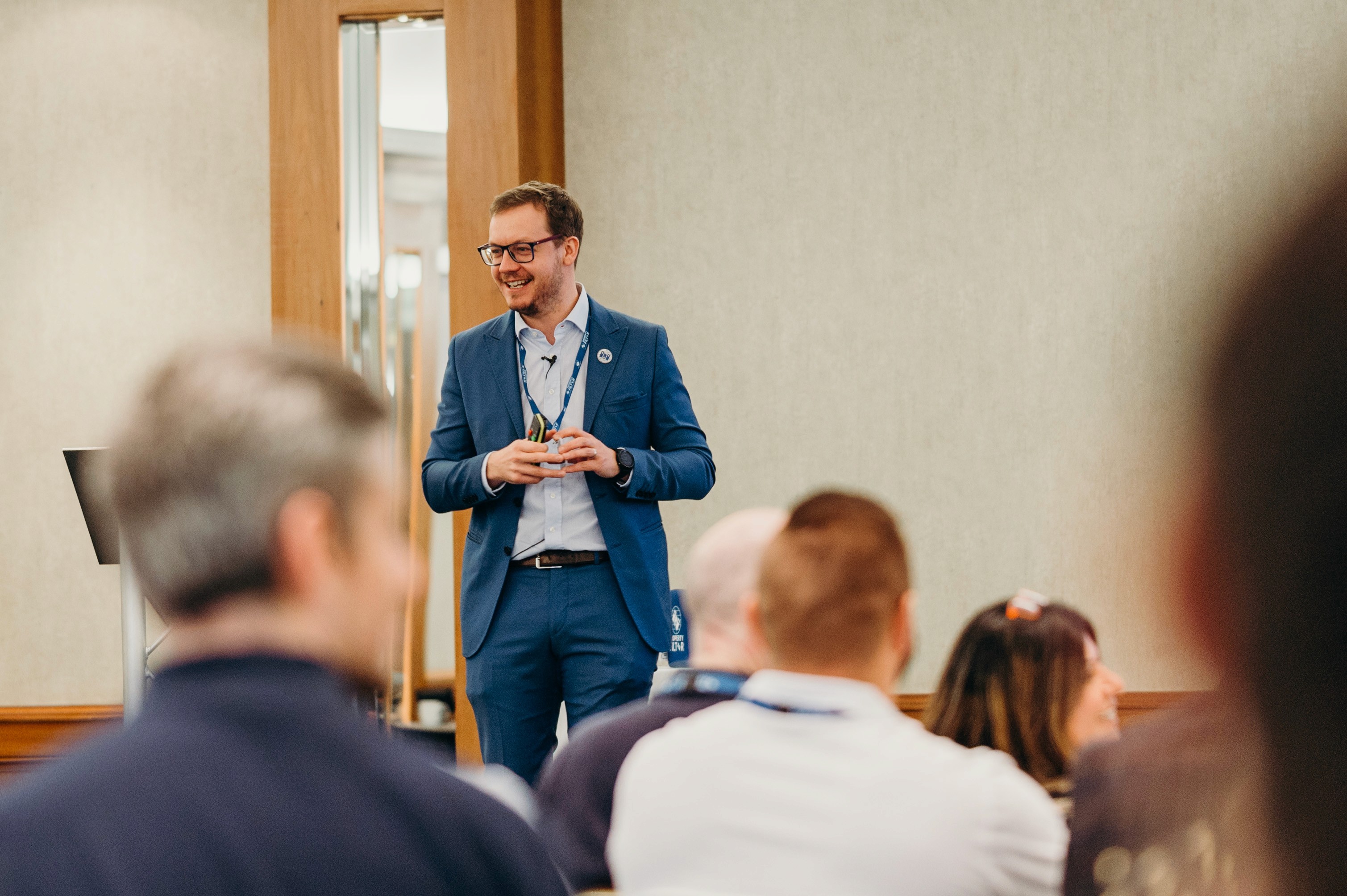 Guillaume Black: Man with glasses and beard wearing blue suit presenting to audience in conference room