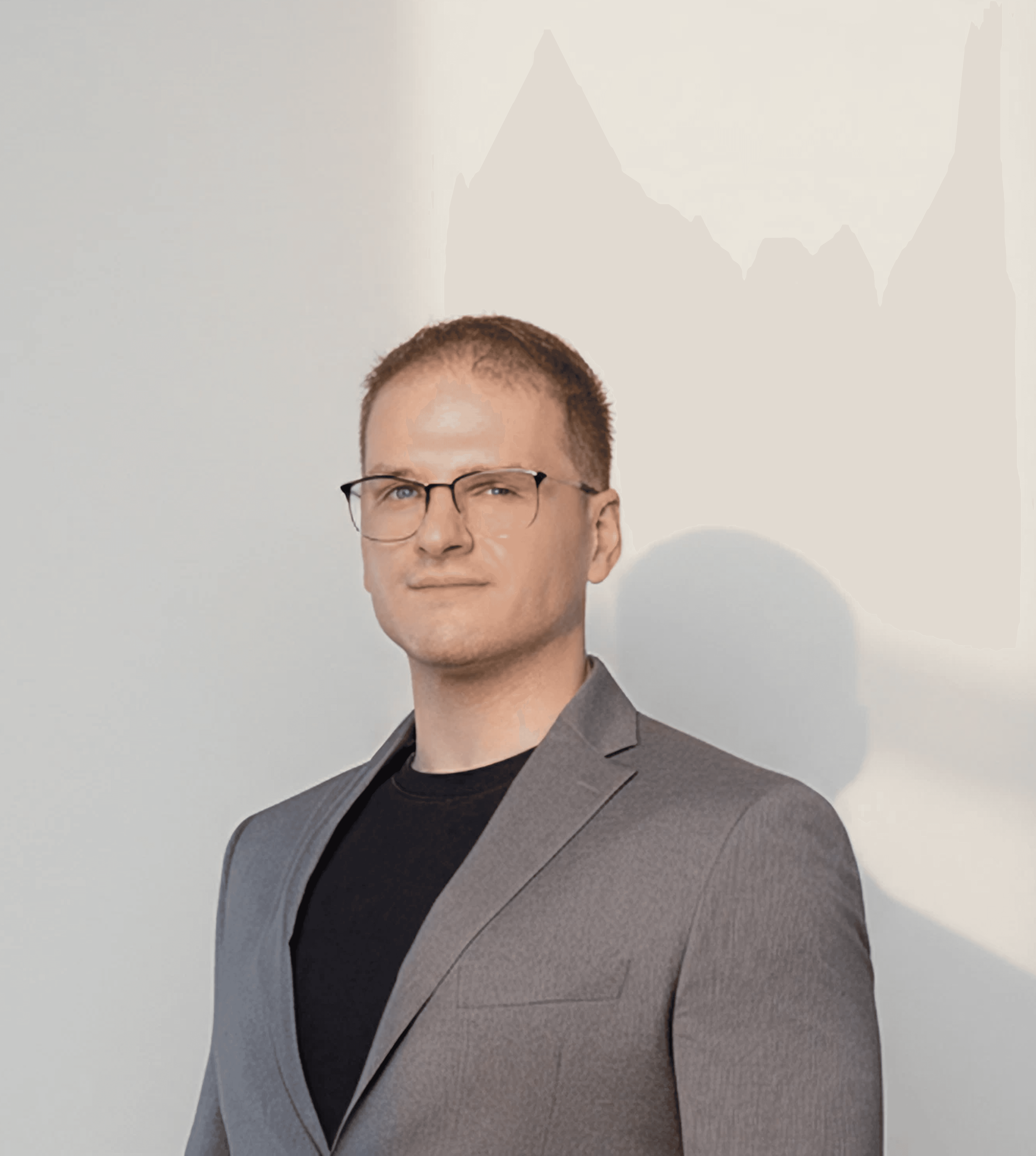 Man in glasses wearing a grey suit and blue tie, looking calmly at the camera.