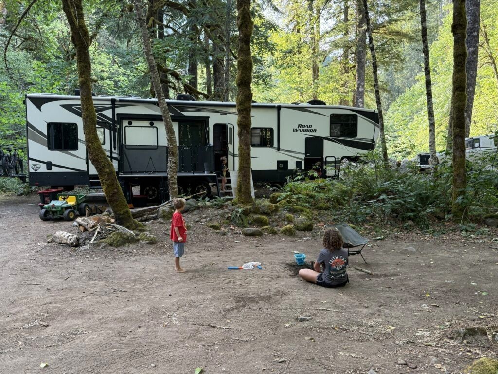 Our RV parked in mossy Pacific Northwest forest with kids playing outside
